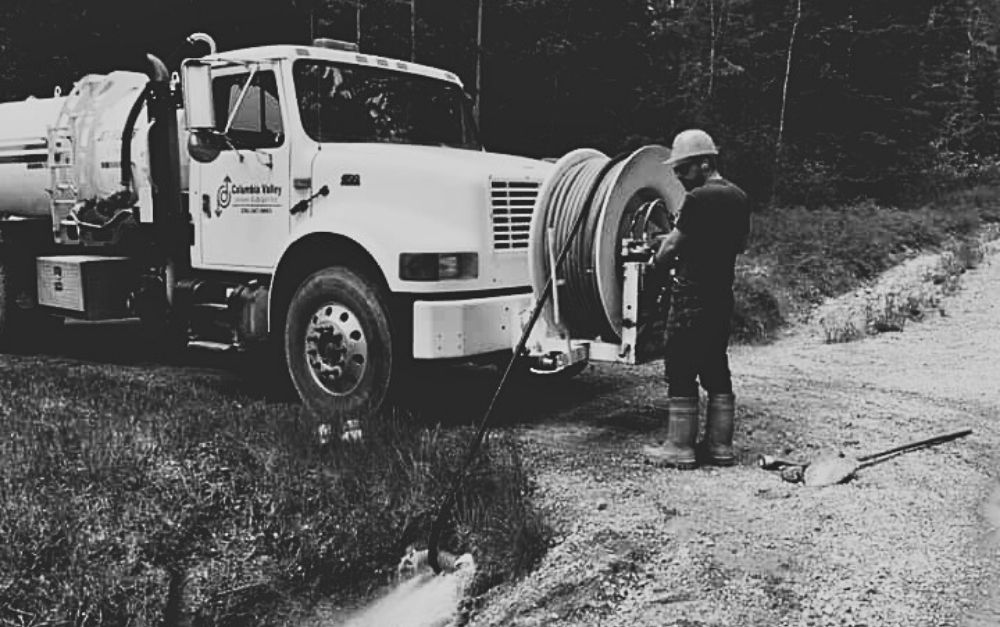 A black and white photo of a man standing next to a vacuum truck.