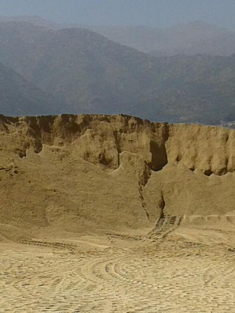 Acantilado arenoso erosionado en un paisaje desértico con montañas en la distancia.