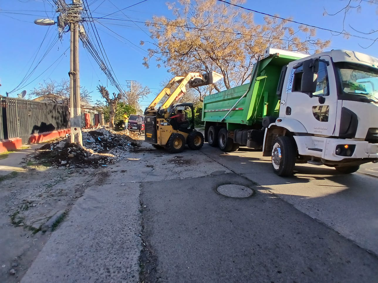 Un minicargador amarillo carga escombros en un camión volquete verde en una calle de la ciudad.