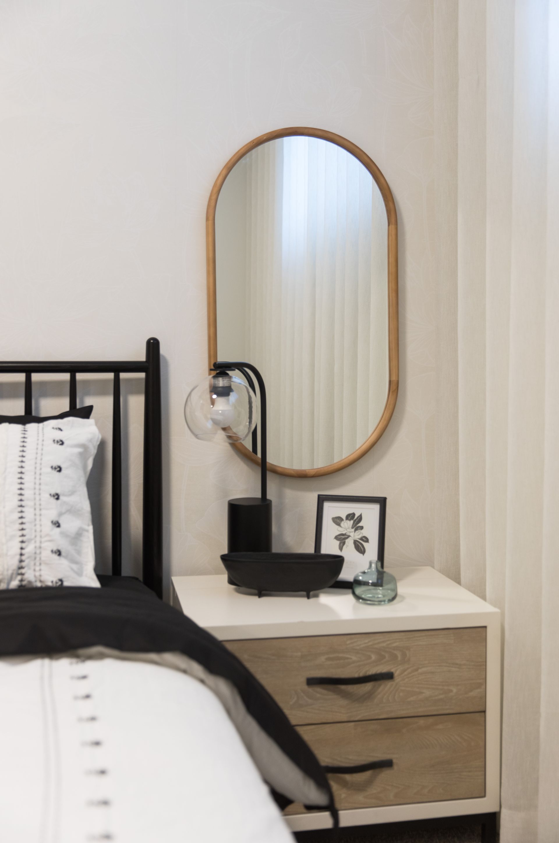 A bedroom with a bed , nightstand , mirror and lamp.