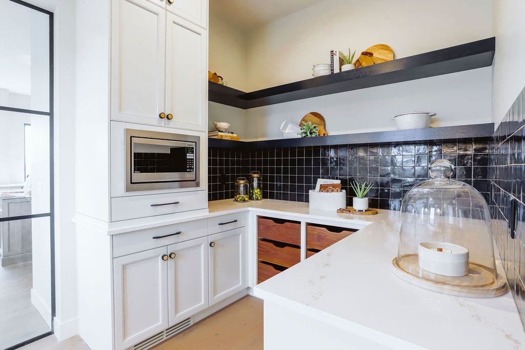 A kitchen with white cabinets , black tiles , a microwave , and a glass door.
