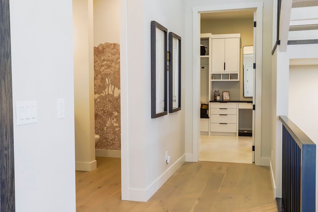 A hallway in a house with hardwood floors and white walls leading to a kitchen.