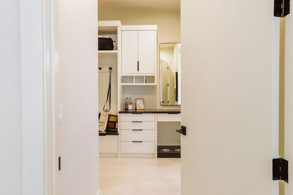A hallway leading to a laundry room with white cabinets and a mirror.
