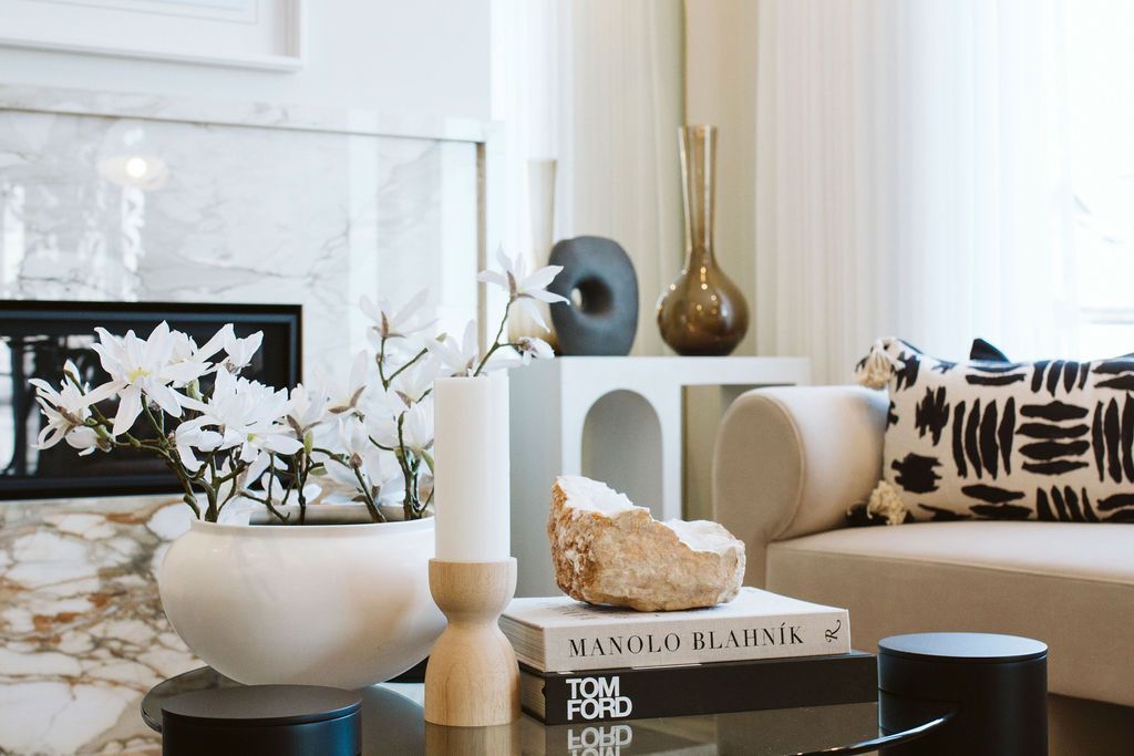 A living room with a couch , coffee table , vases and a fireplace.