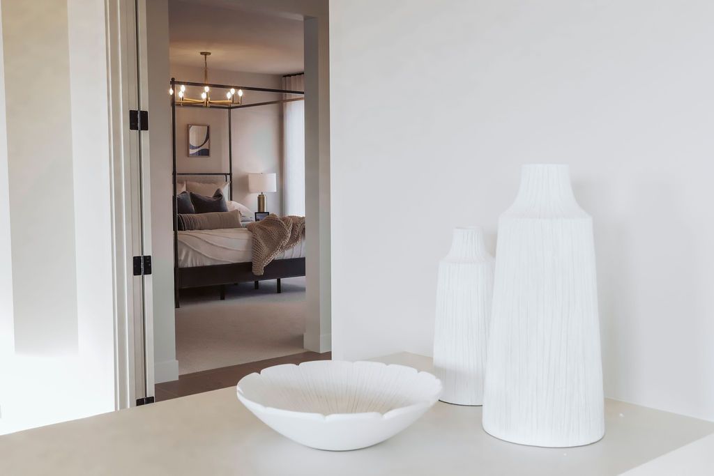 A bedroom with a canopy bed and a bowl and vases on a table.