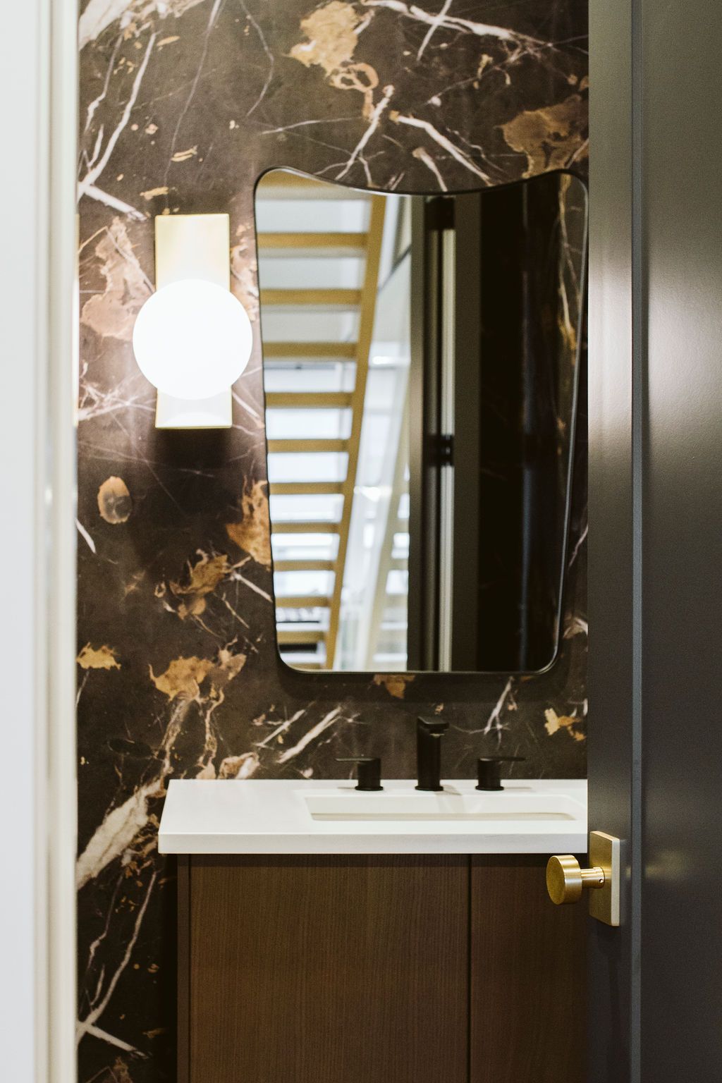 A bathroom with a sink and a mirror with a staircase in the background