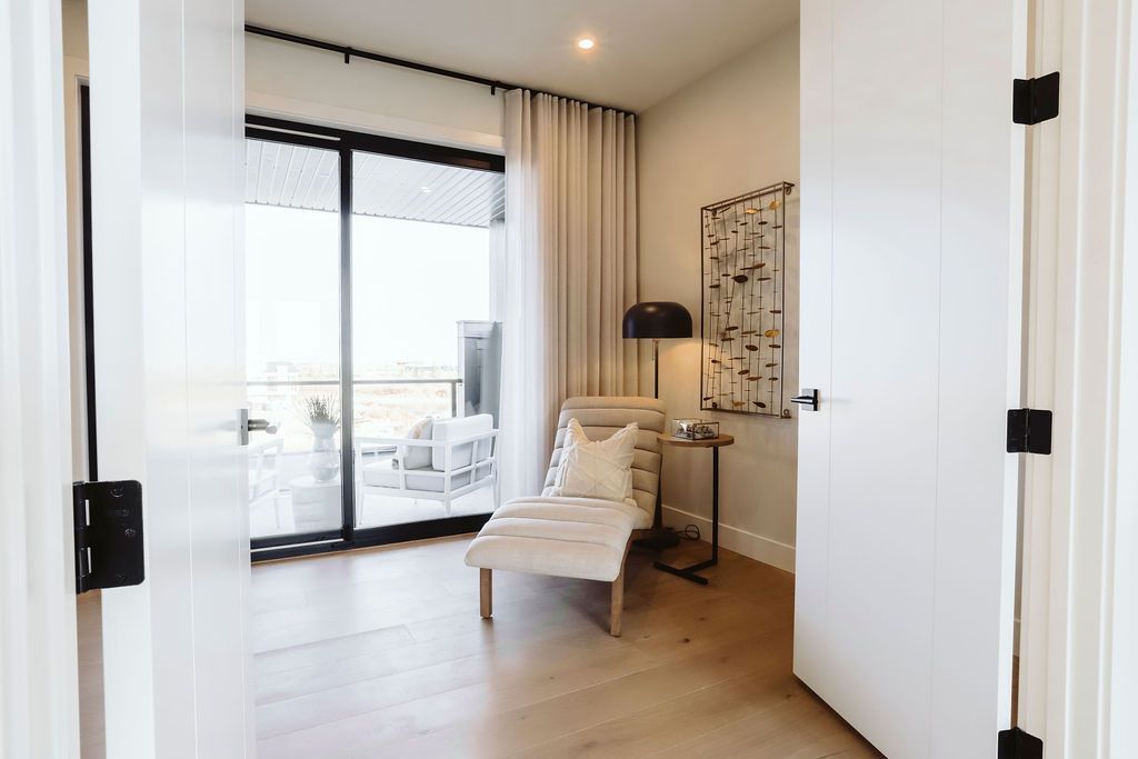 A bedroom with a chair , table , lamp and sliding glass doors.