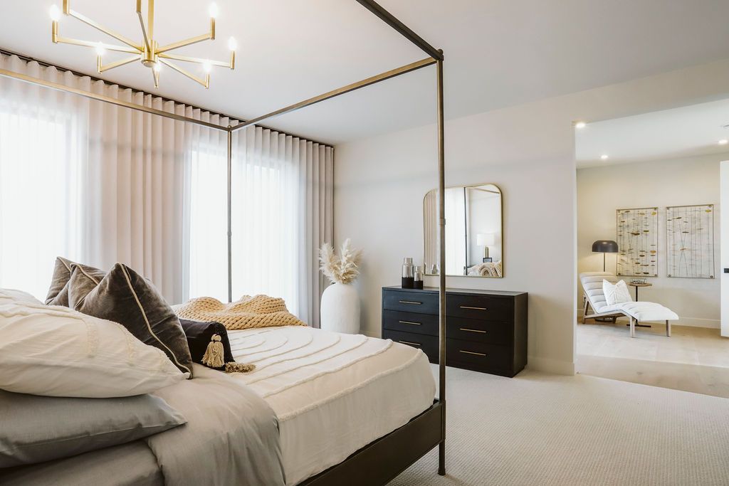 A bedroom with a four poster bed , dresser , mirror and chandelier.
