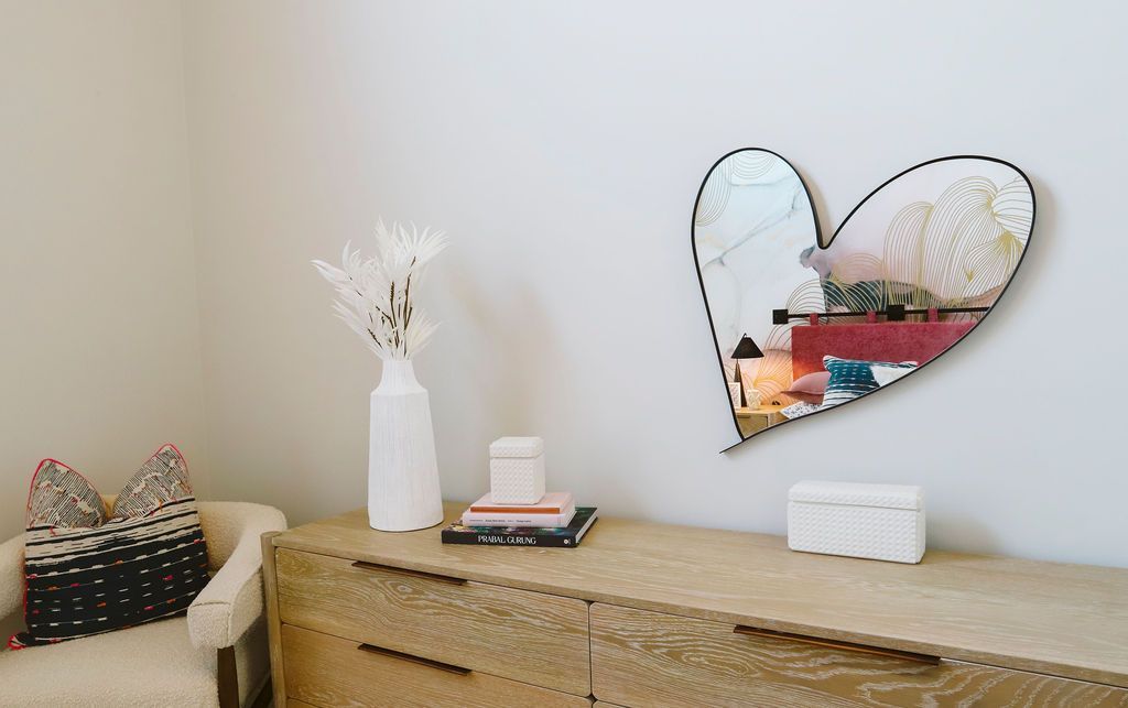 A heart shaped mirror is hanging on a wall next to a dresser.