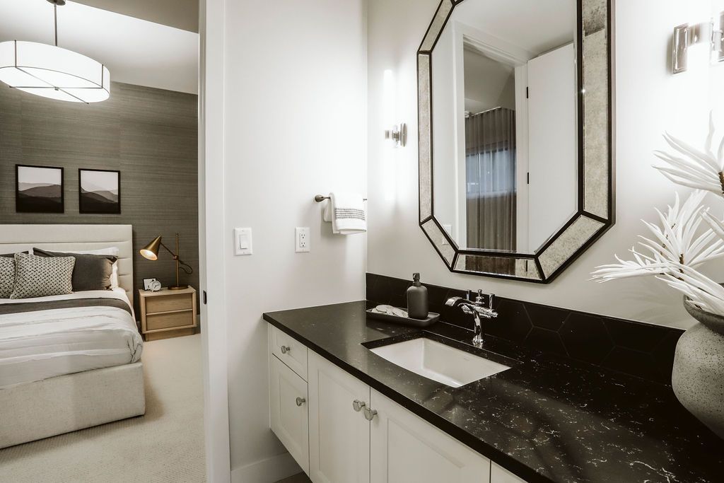 A bathroom with a sink and a mirror next to a bedroom.