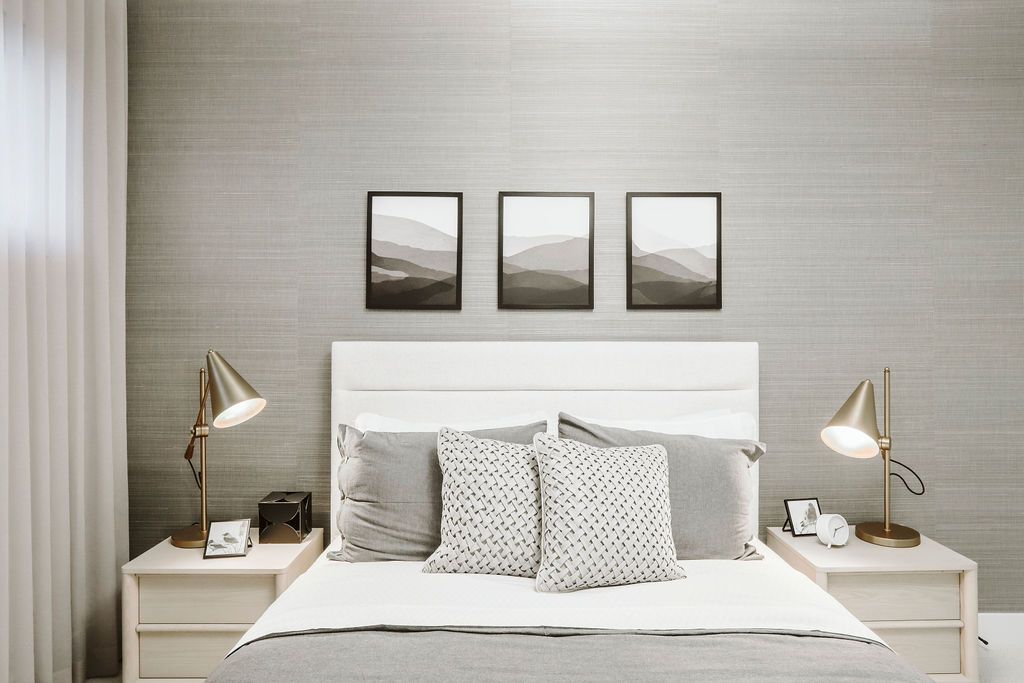 A bedroom with a bed , two nightstands , two lamps and three pictures on the wall.