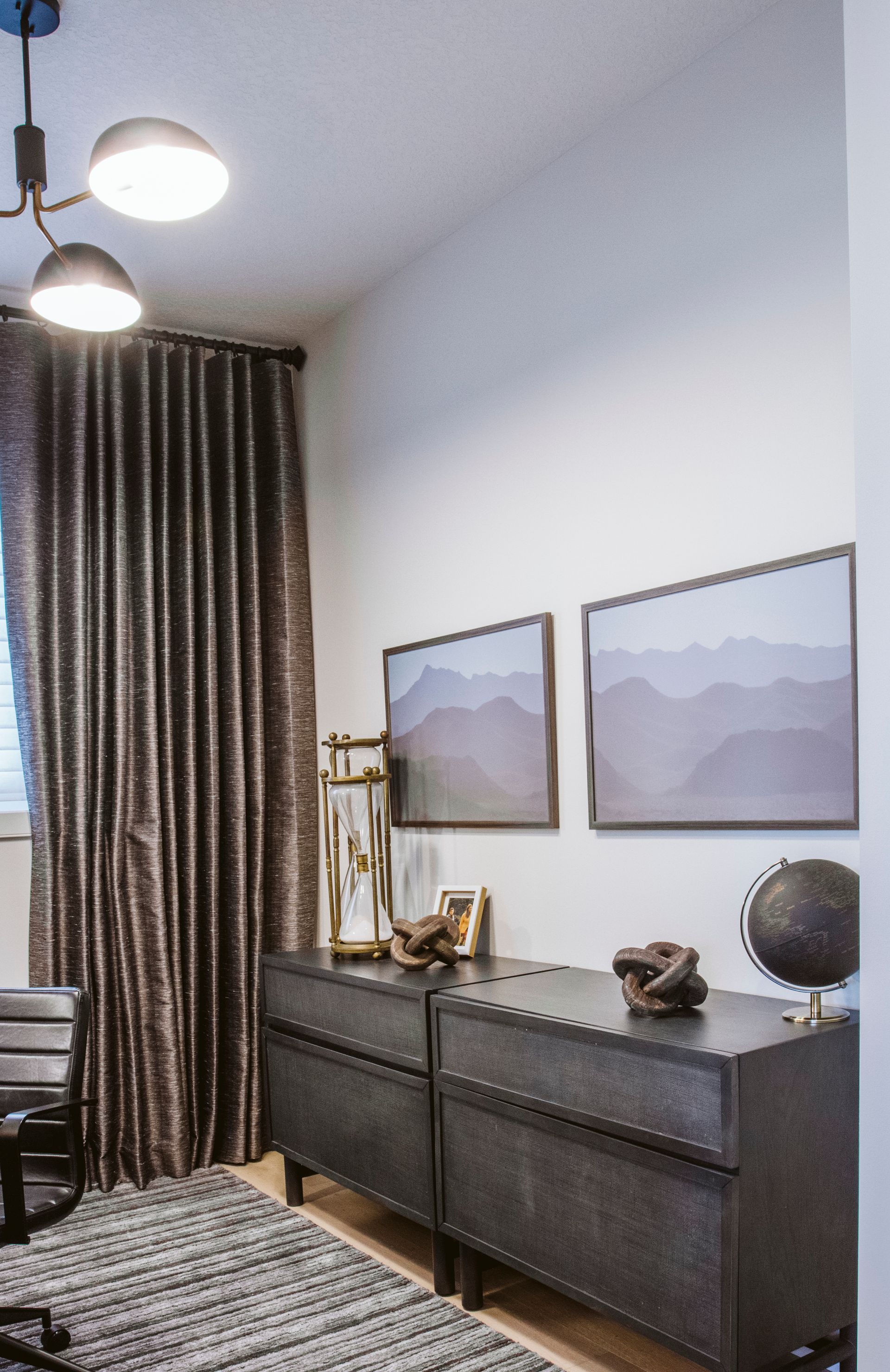 A room with a dresser , chair , globe and paintings on the wall.