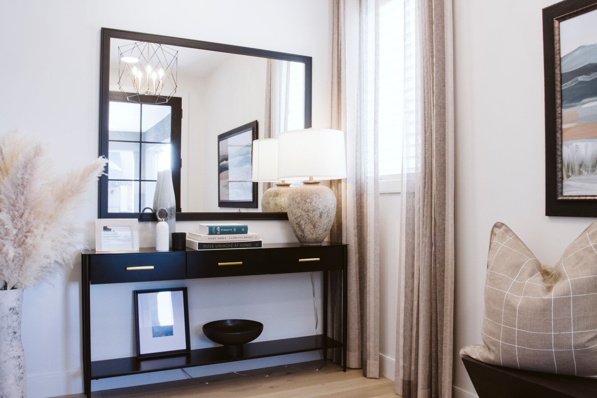 A living room with a table , mirror , lamps , and pictures.