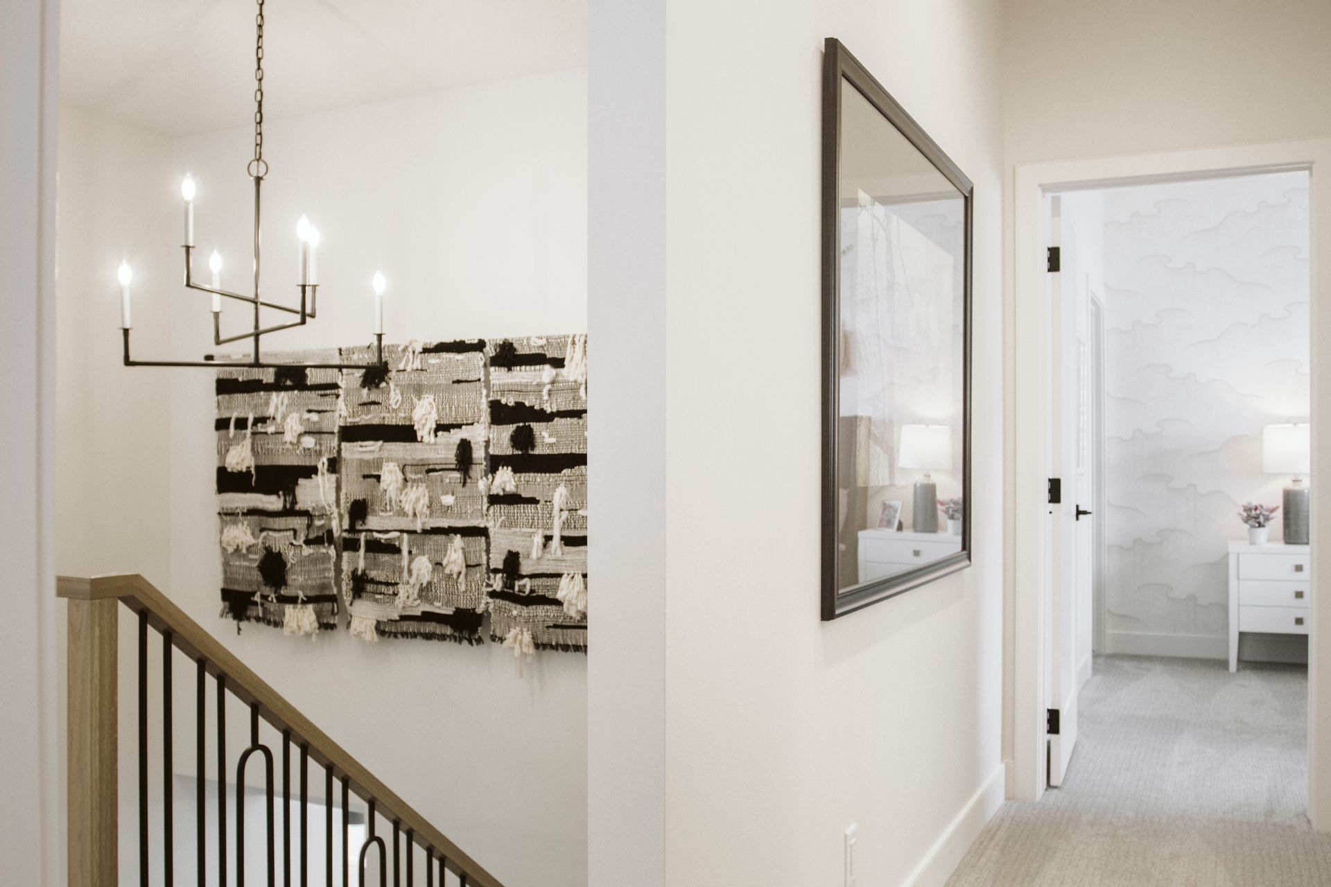 A hallway with a staircase , a mirror and a painting on the wall.