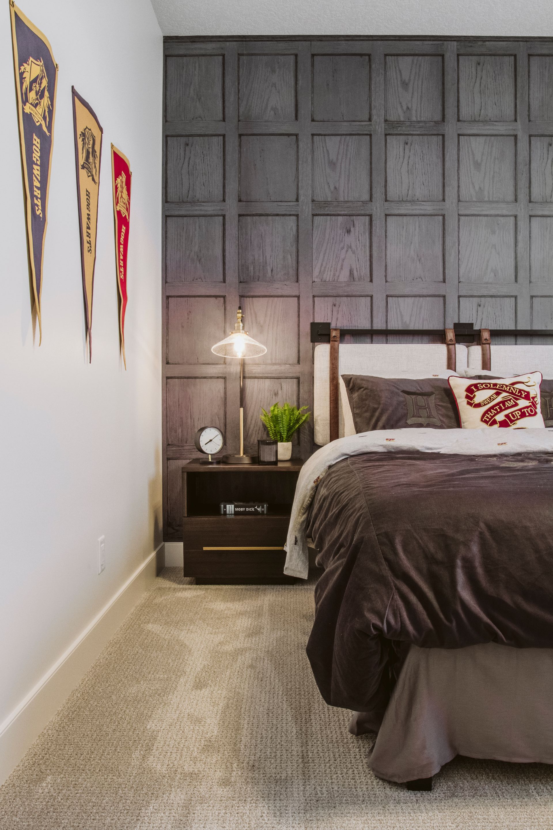A bedroom with a bed , nightstand , lamp and flags on the wall.