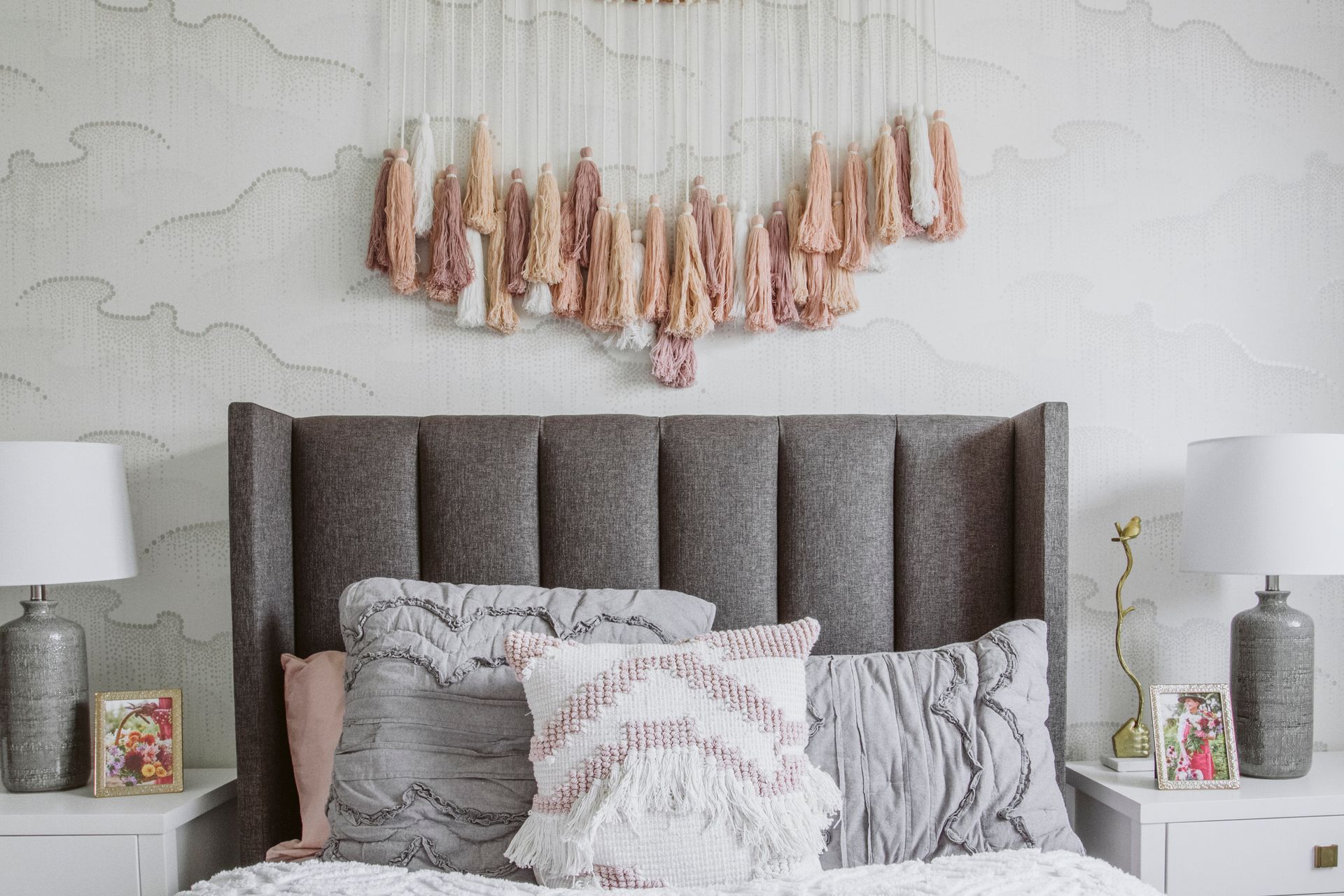 A bedroom with a bed , nightstands , lamps and a wall hanging.