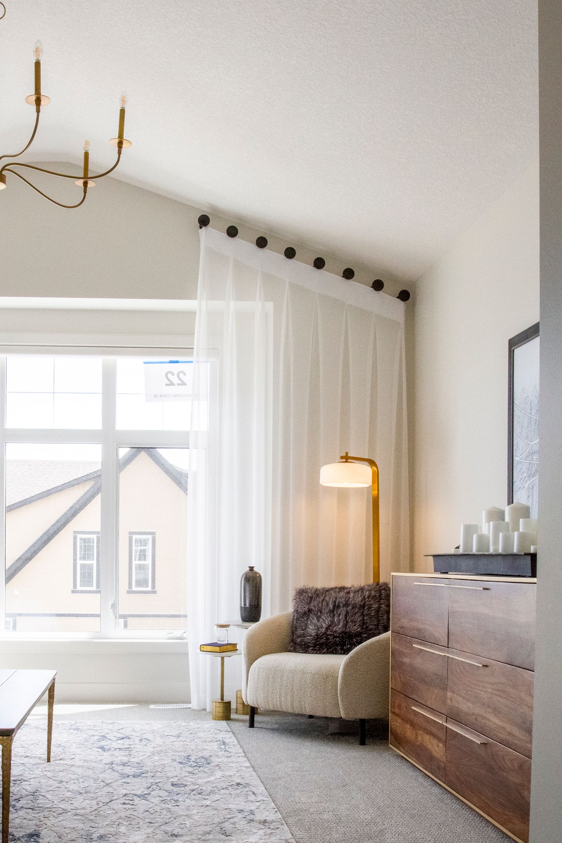A living room with a chair , dresser , lamp and window.