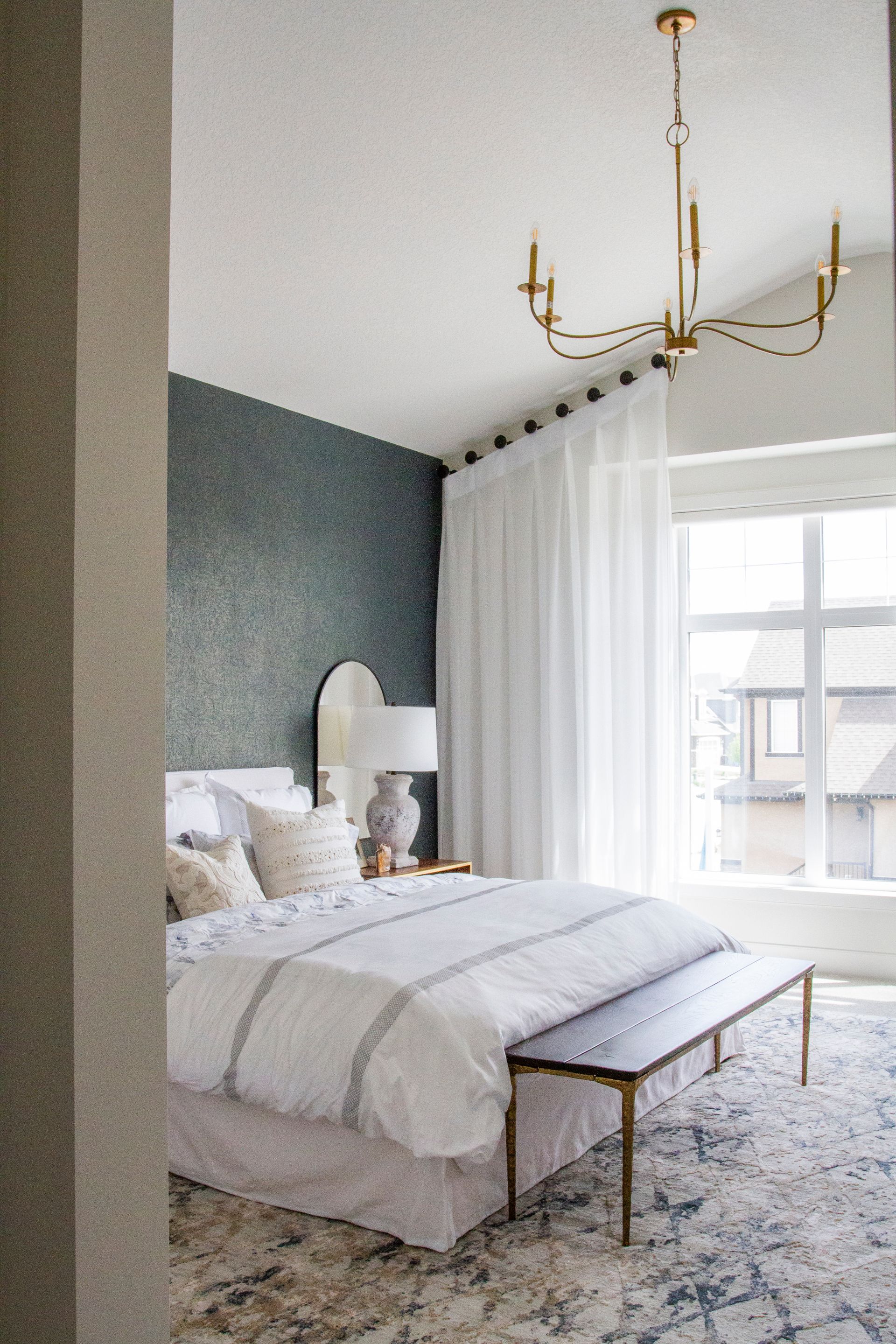 A bedroom with a bed , bench , chandelier and window.