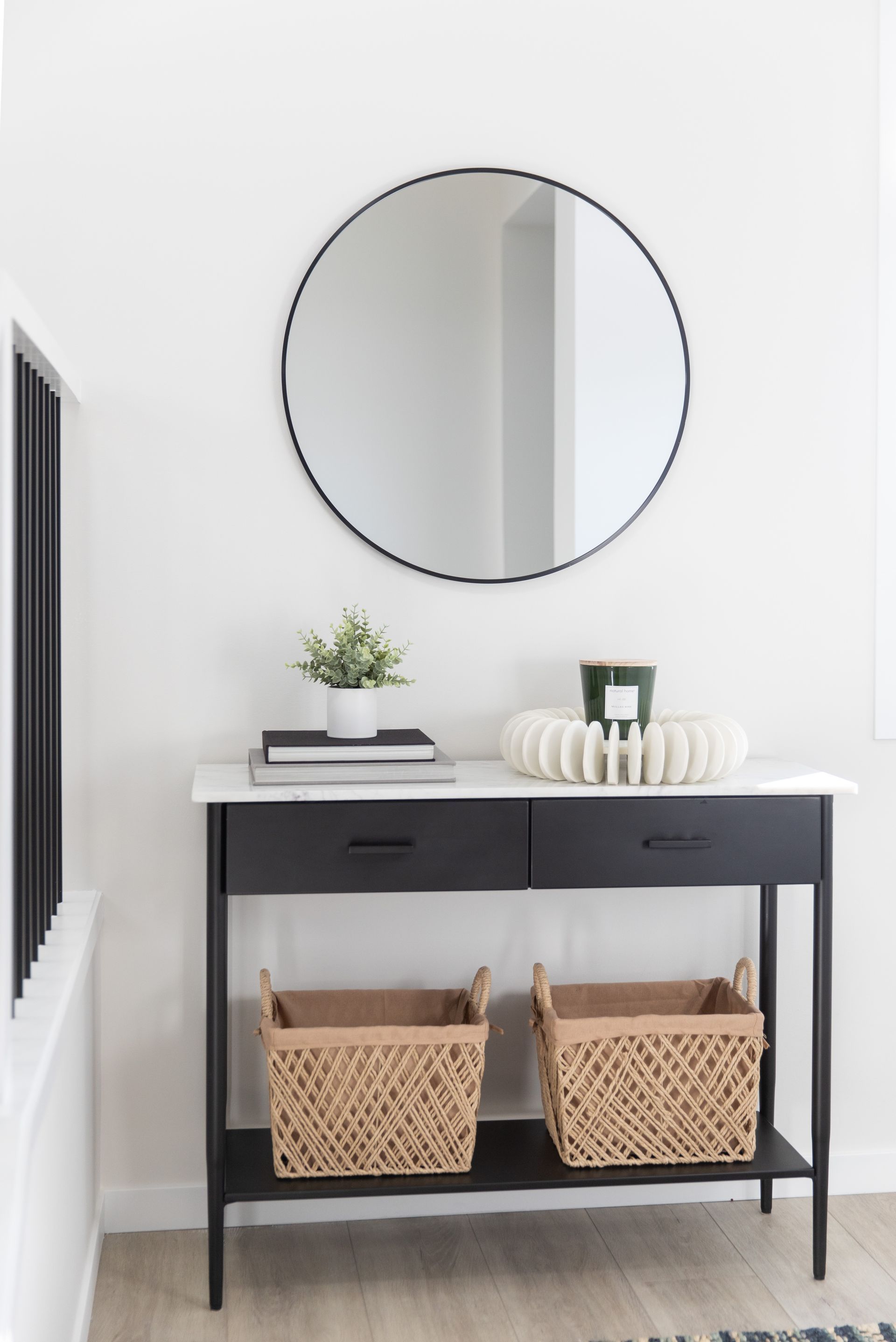 A black console table with two baskets underneath a round mirror.
