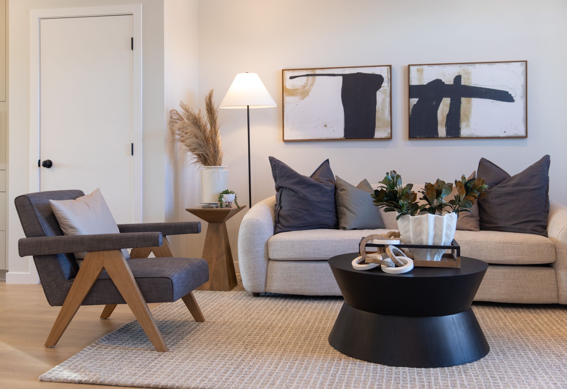 A living room with a couch , chair , coffee table and paintings on the wall.