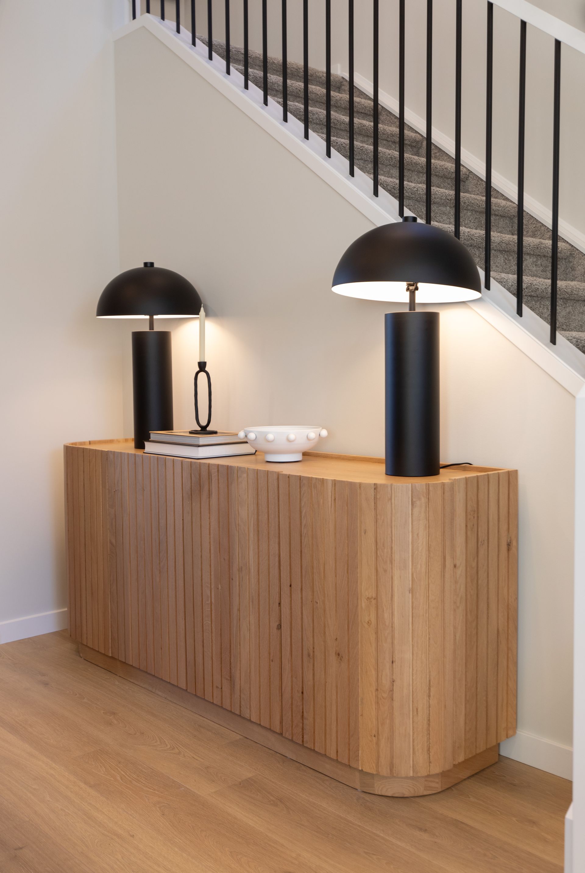 Two black lamps are sitting on a wooden table next to a staircase.
