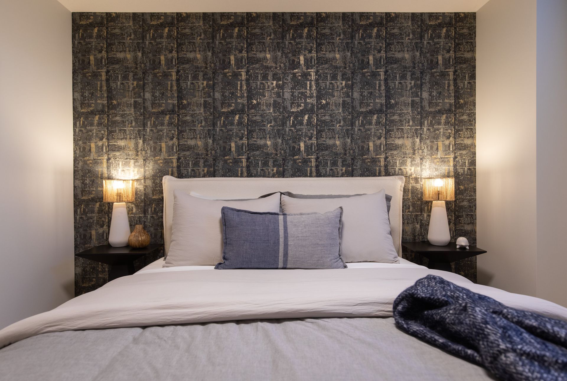 A bedroom with a bed , two lamps , and a wall with a patterned wallpaper.