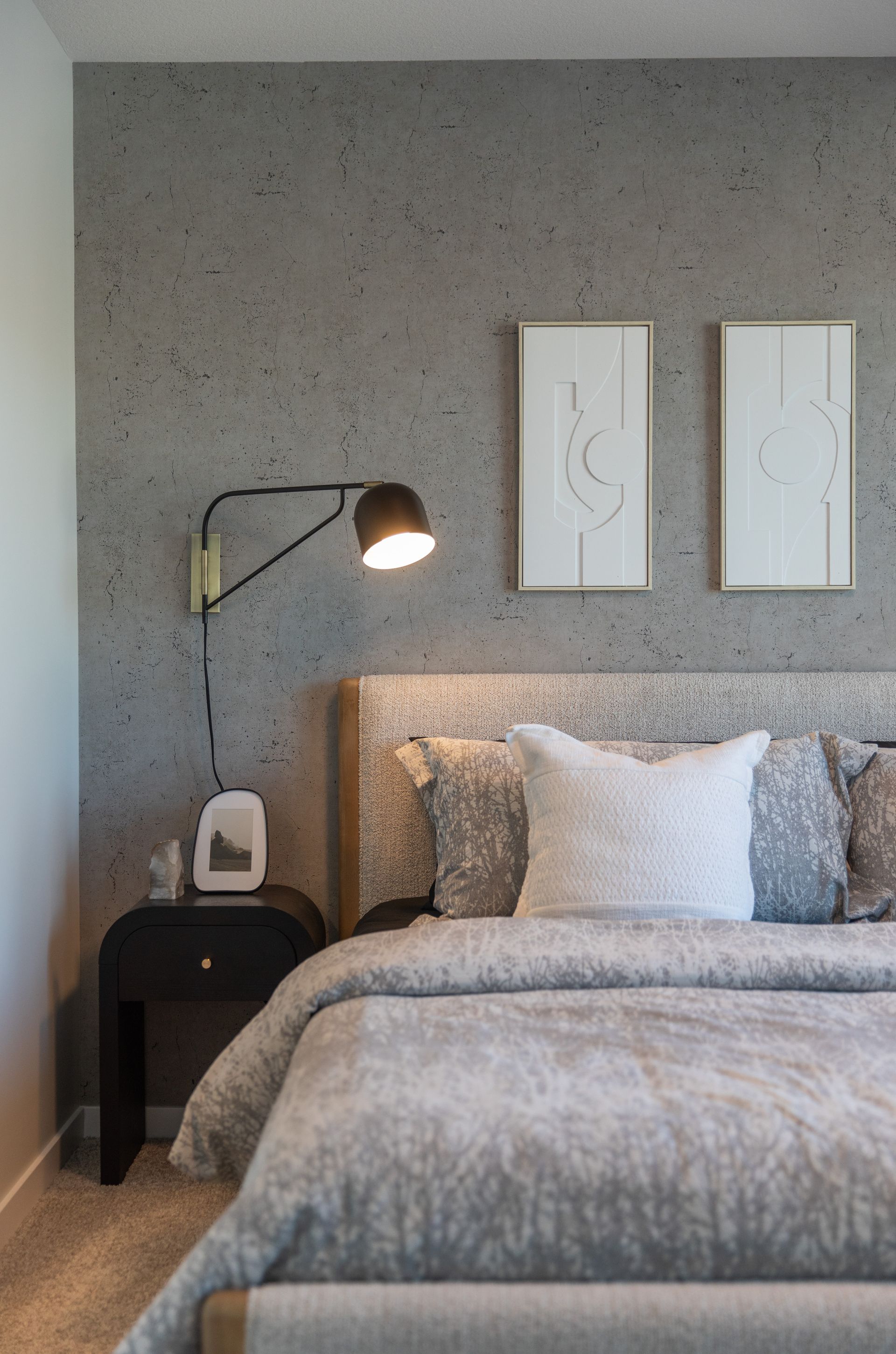 A bedroom with a bed , nightstand , lamp and two paintings on the wall.