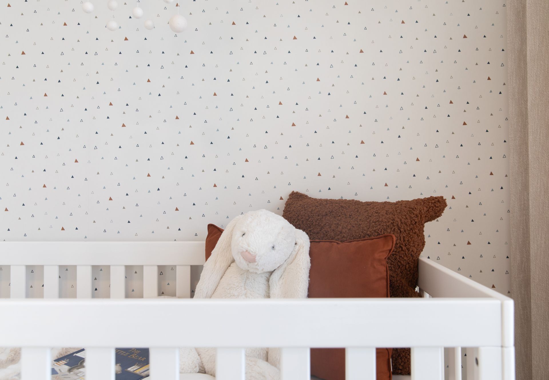 A teddy bear is sitting in a white crib in a nursery.