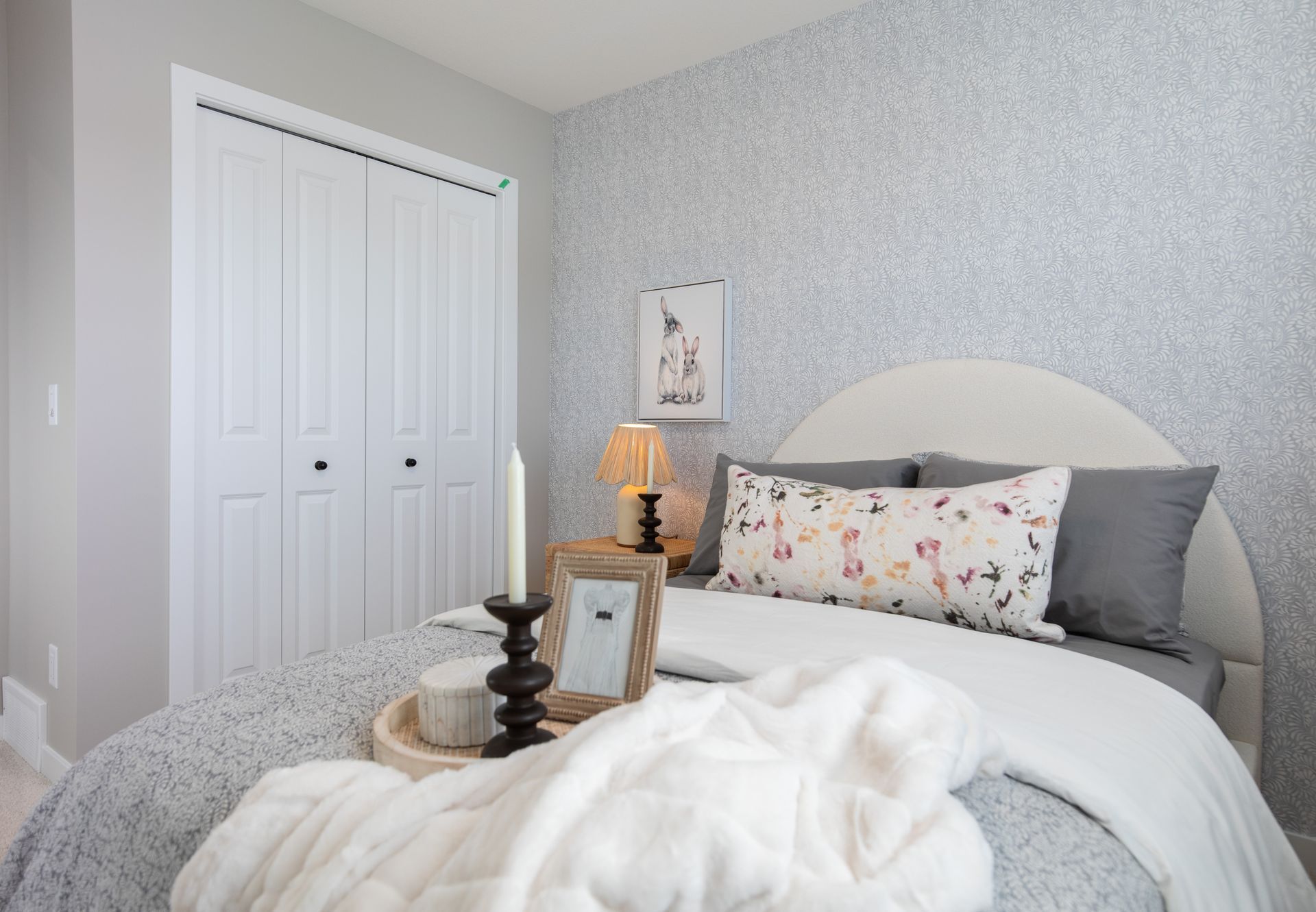 A bedroom with a bed , nightstand , candles and a dresser.