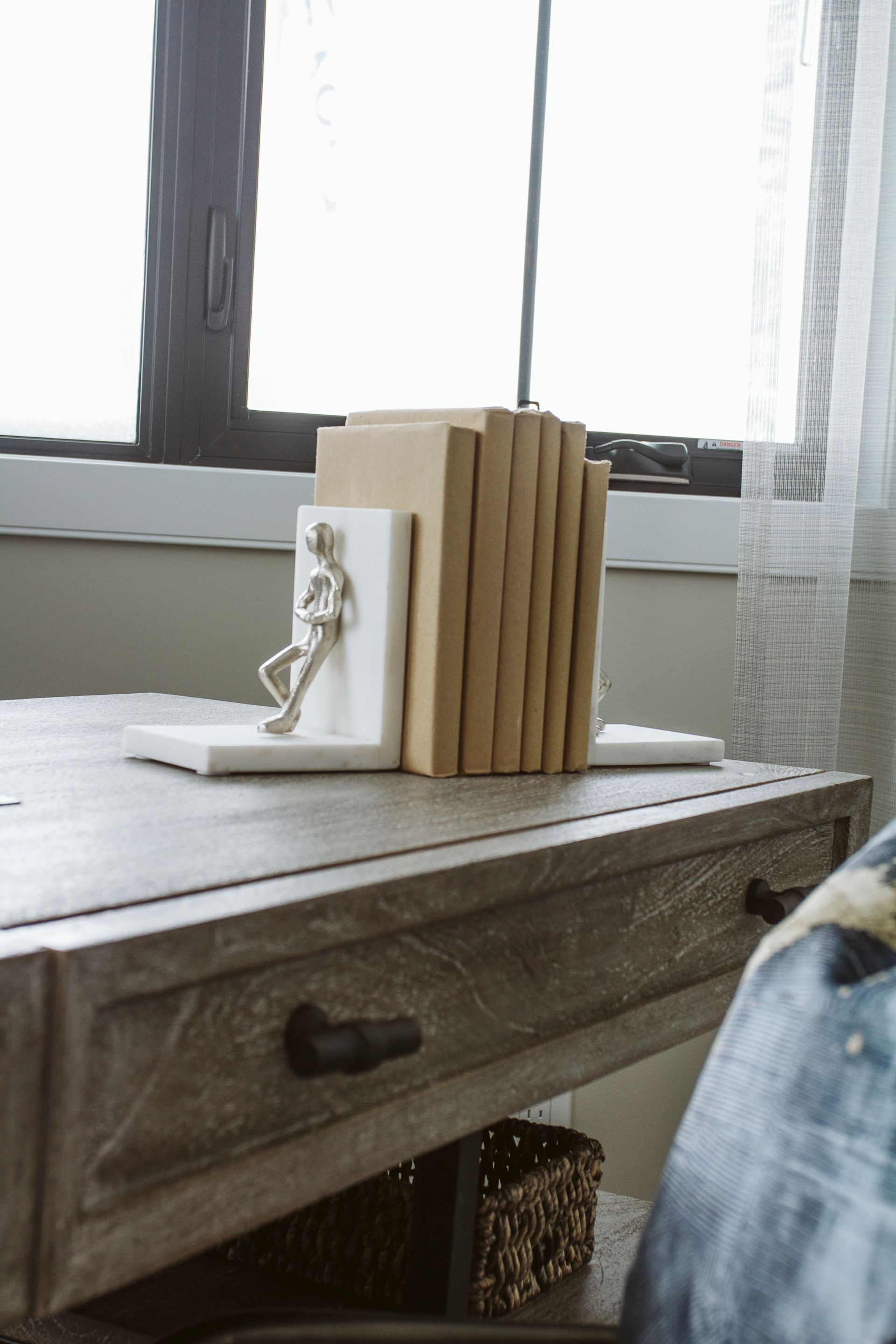 A stack of books sitting on top of a wooden desk next to a window.