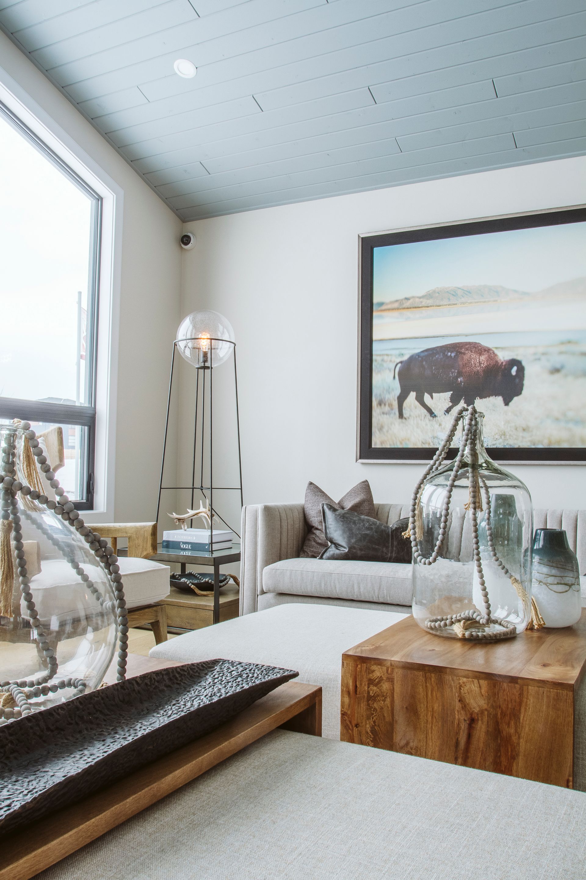 A living room with a couch , table , vases and a painting of a bison on the wall.