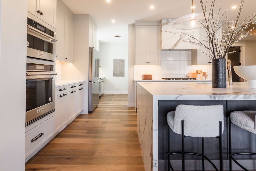 A kitchen with white cabinets , stainless steel appliances , hardwood floors and a large island.