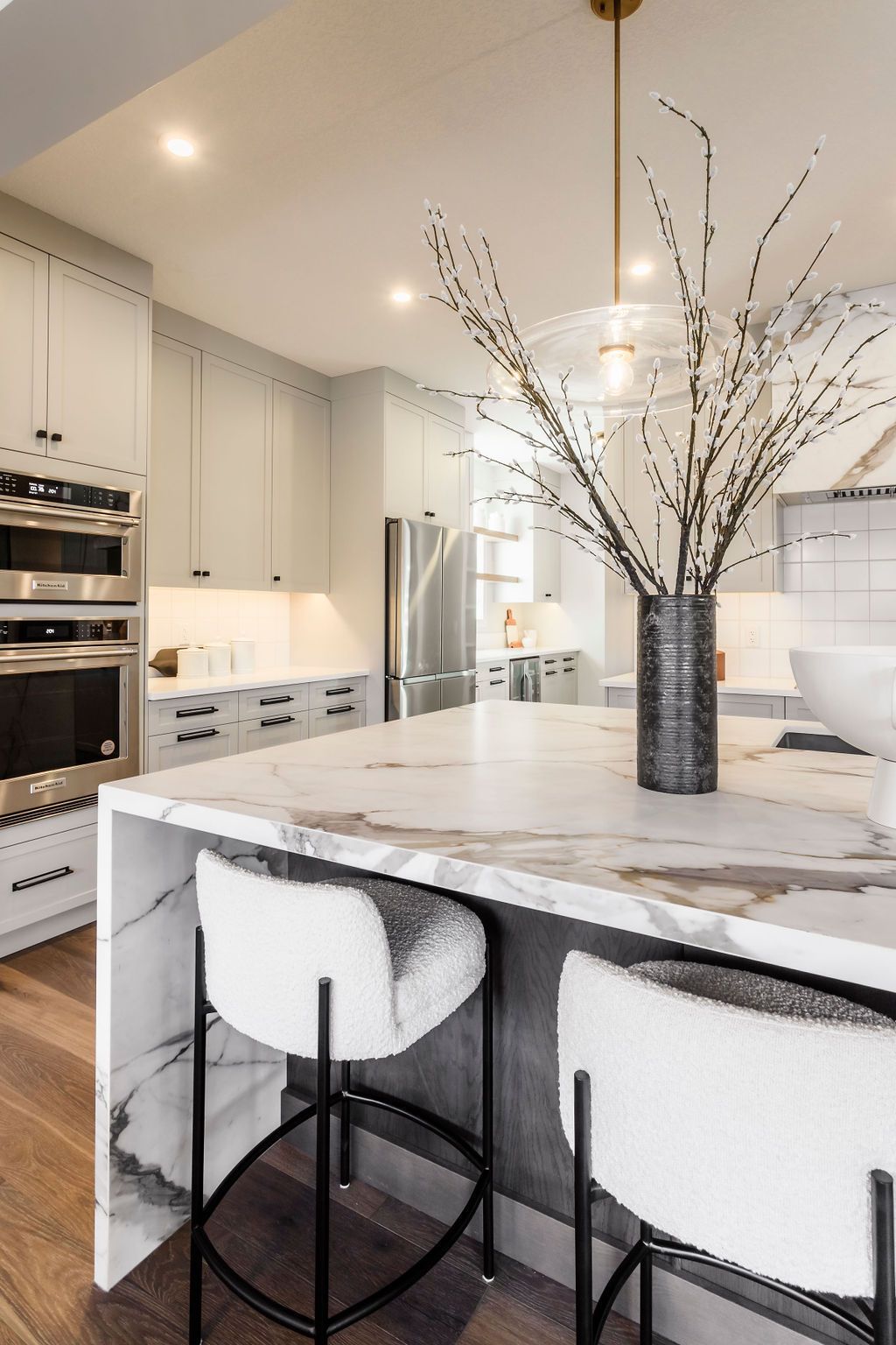 A kitchen with a large island and stools and a vase of branches on the counter.