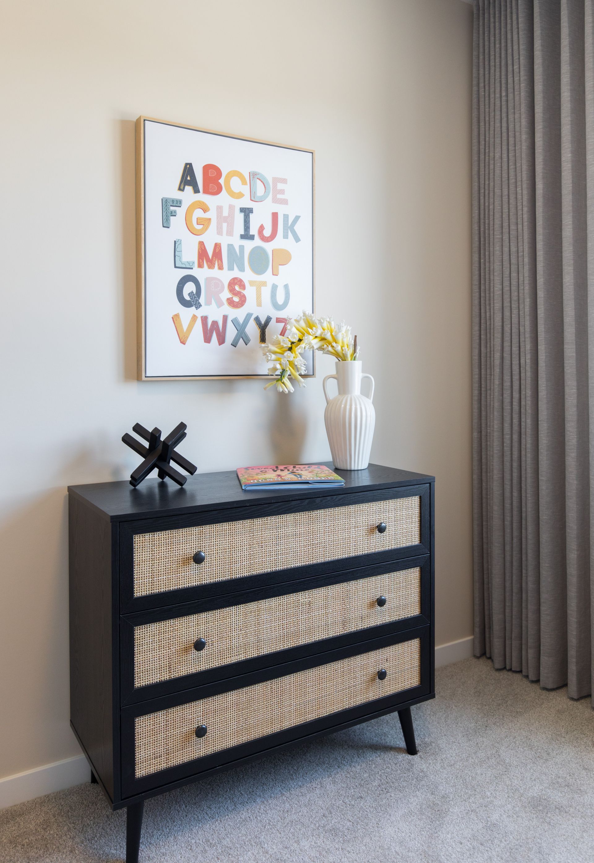 A dresser with a picture of the alphabet on the wall above it.