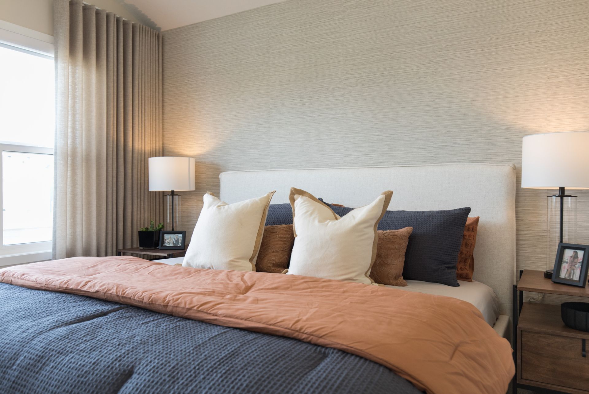 A bedroom with a bed , nightstand , lamp and window.