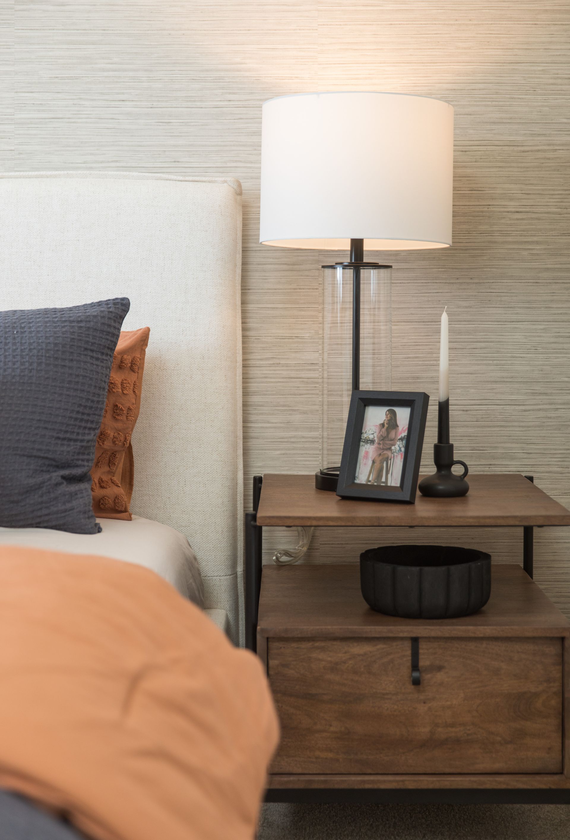 A bedroom with a bed , nightstand , lamp and picture frame