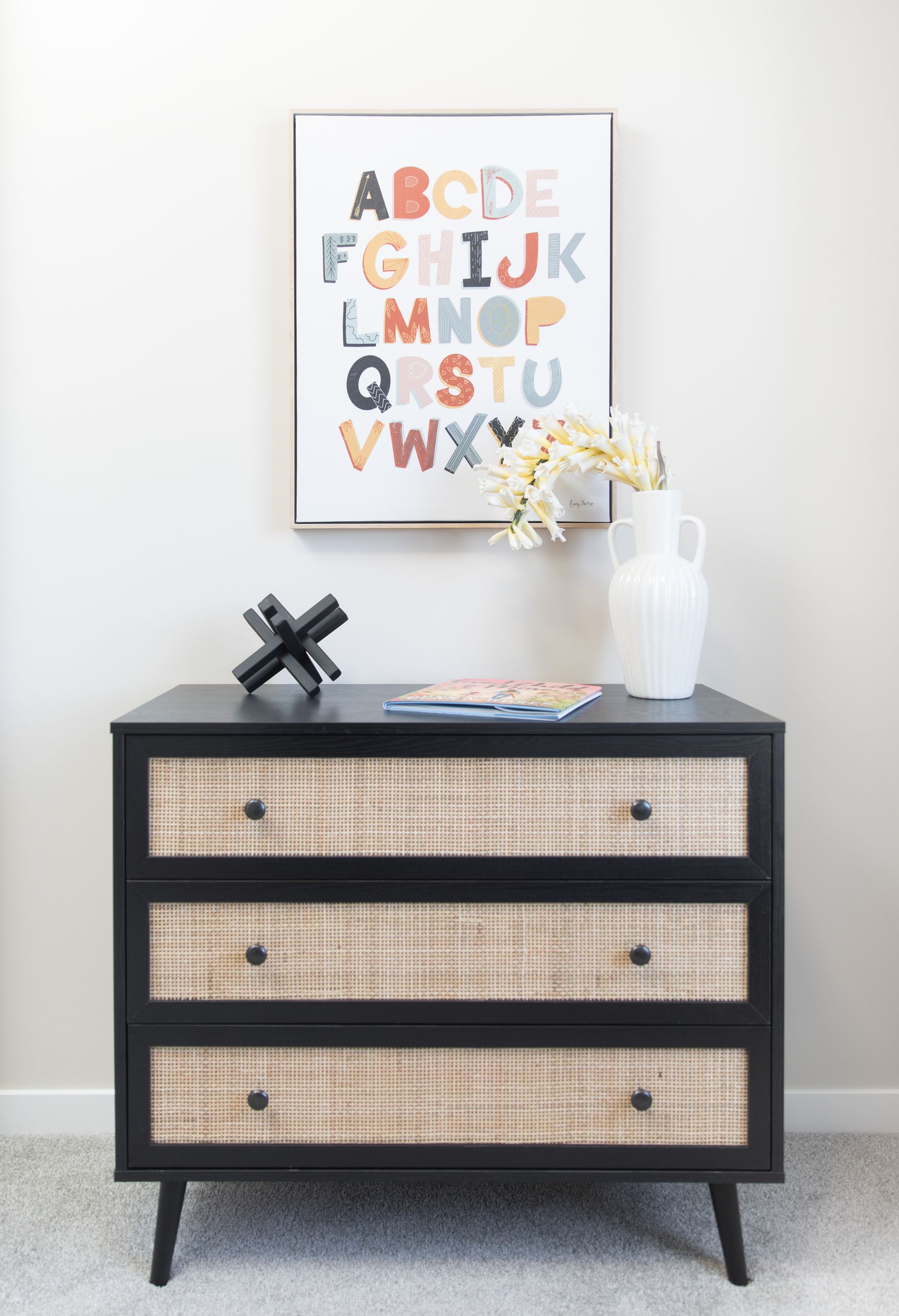 A dresser with a picture of the alphabet on the wall above it.