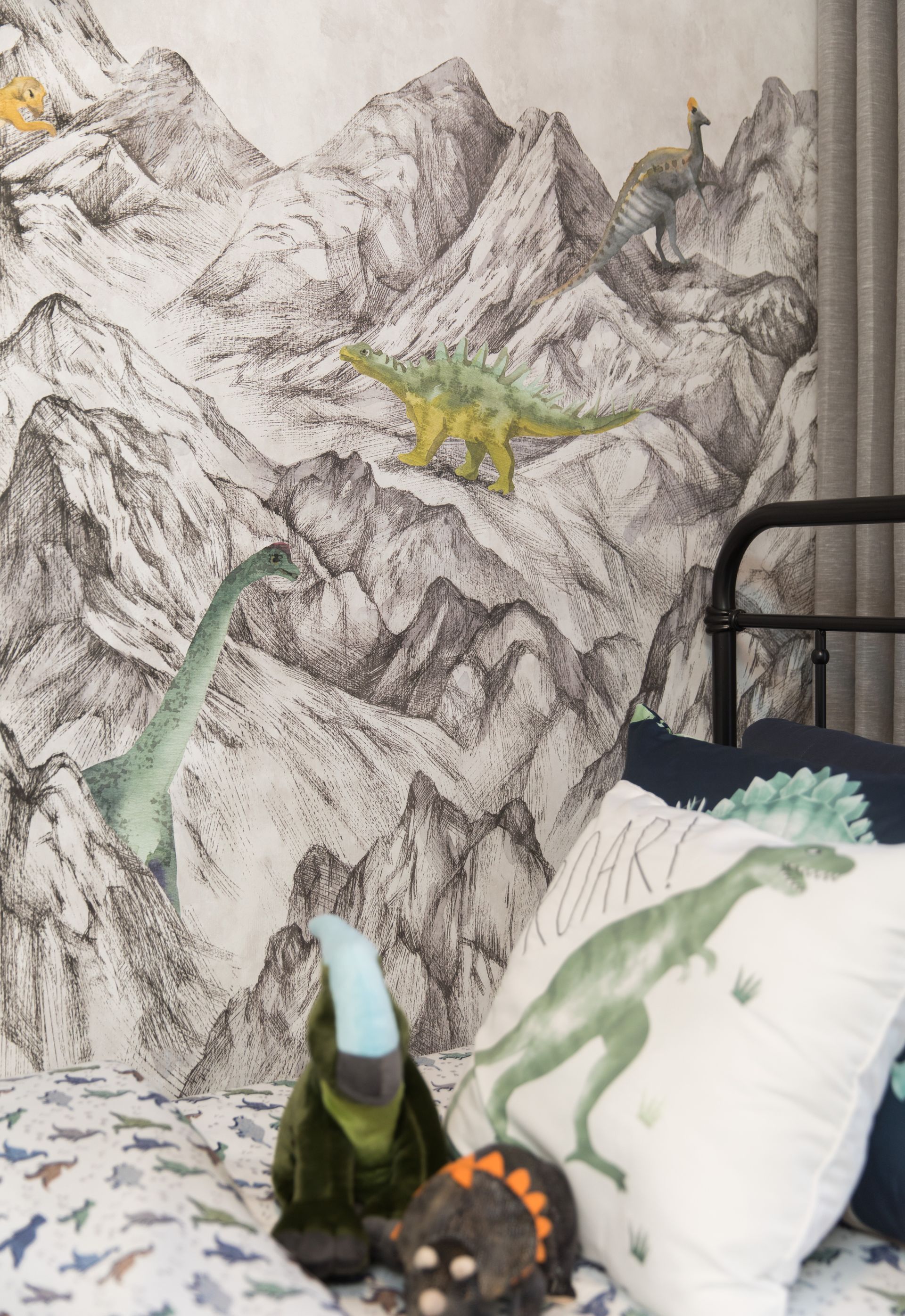 A bed with a painting of dinosaurs on the wall behind it