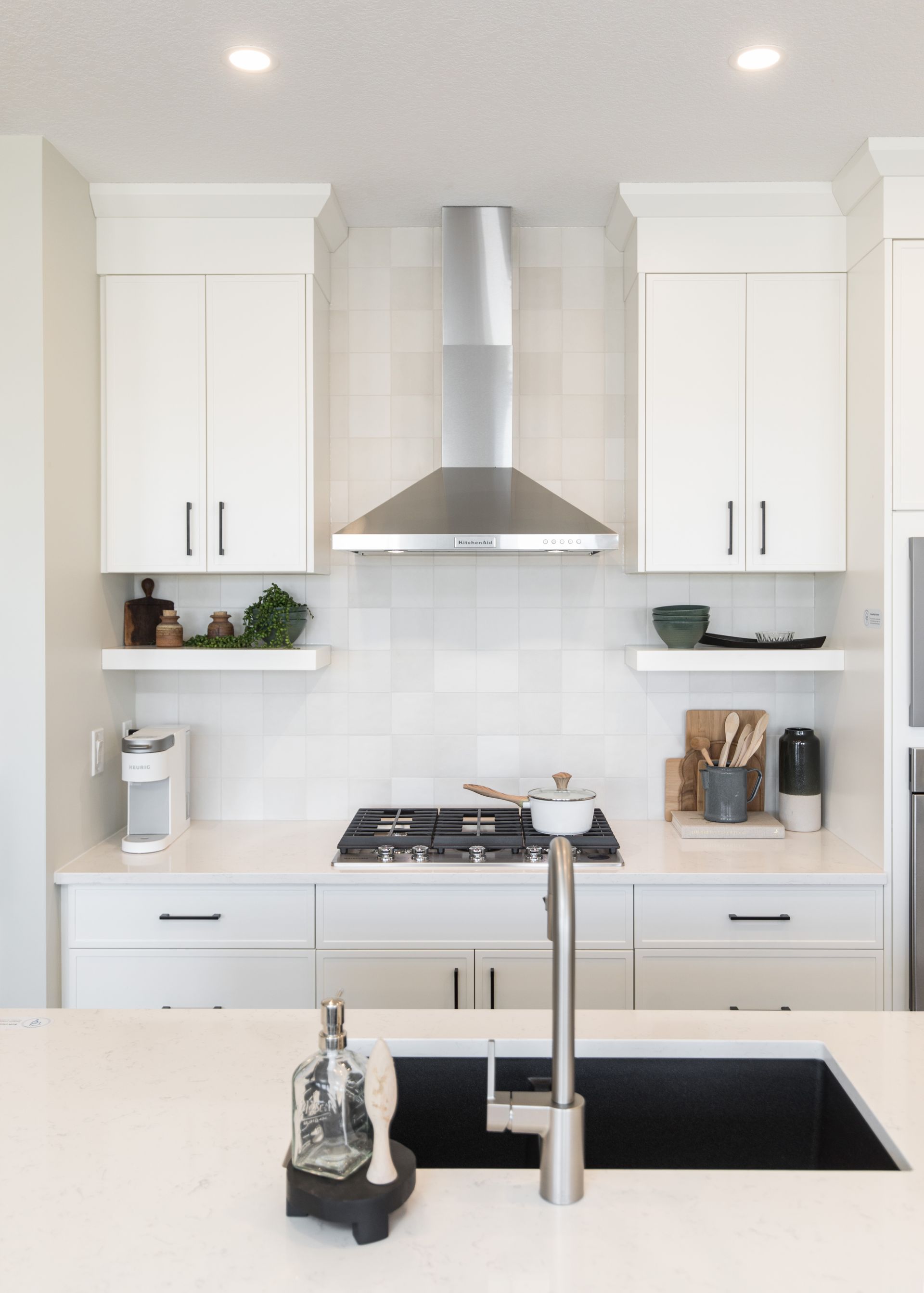 A kitchen with white cabinets , a stove , a sink and a hood.