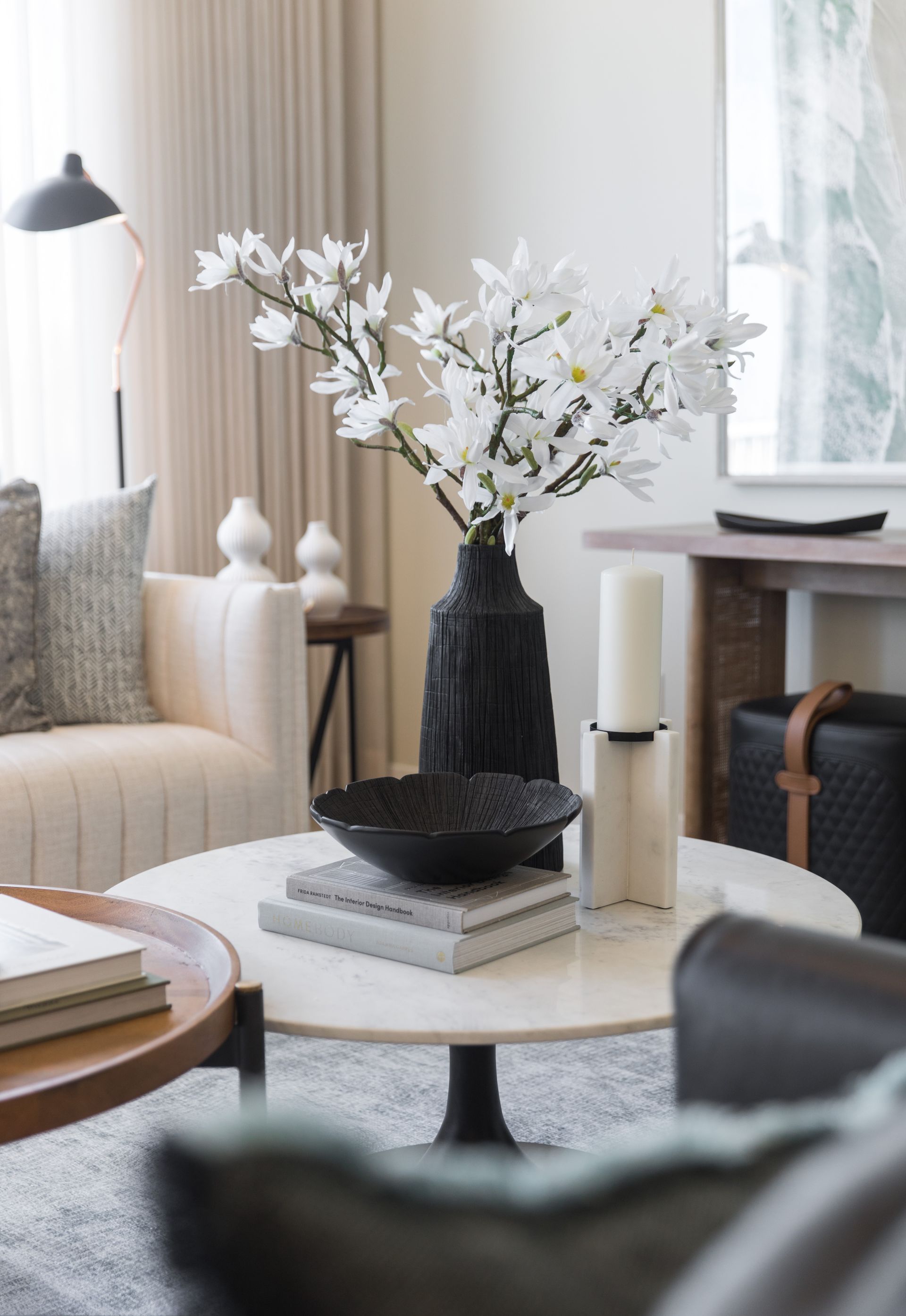 A living room with a couch , chair , coffee table , vase of flowers and candles.