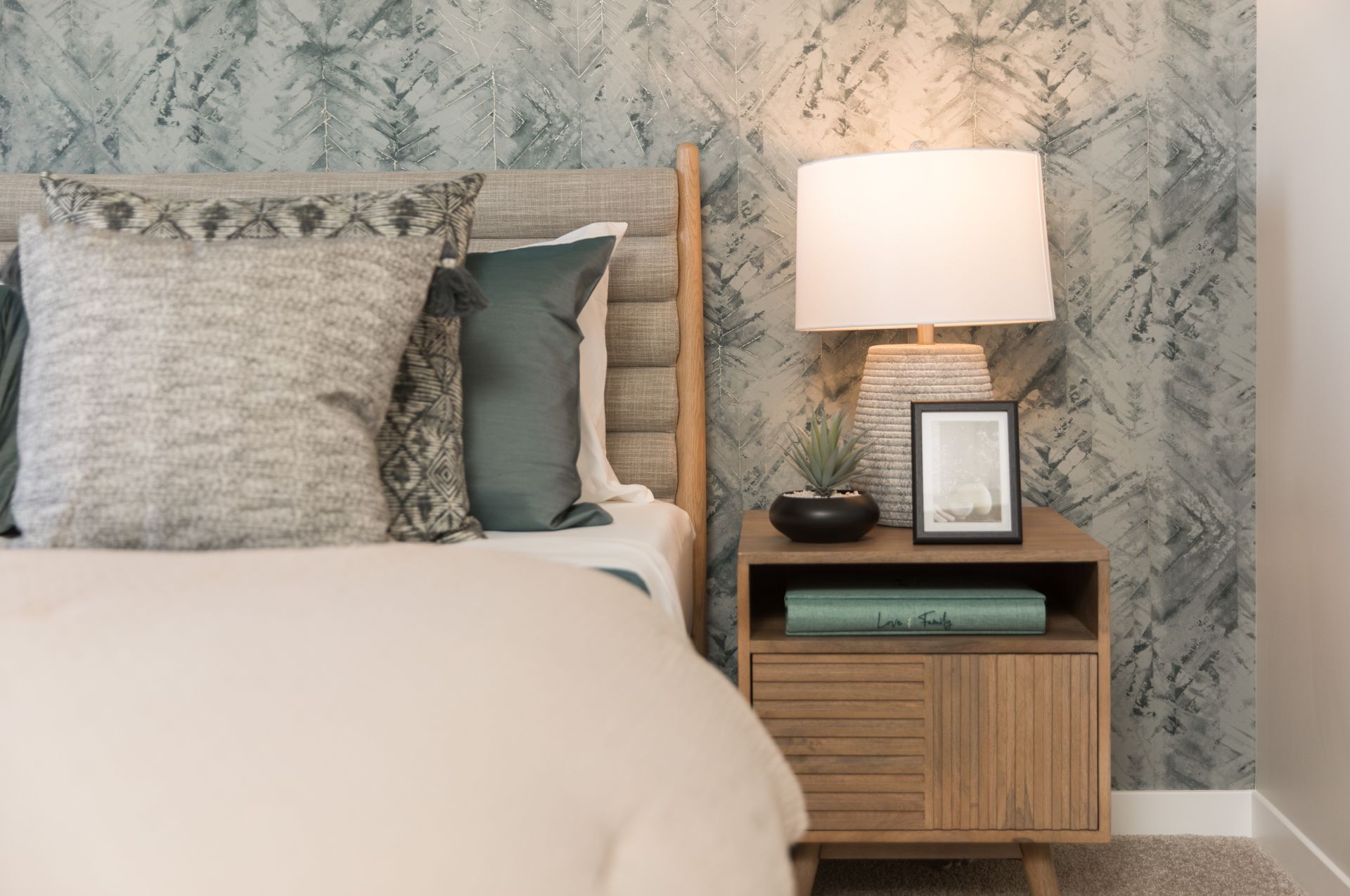 A bedroom with a bed , nightstand , lamp and picture frame.