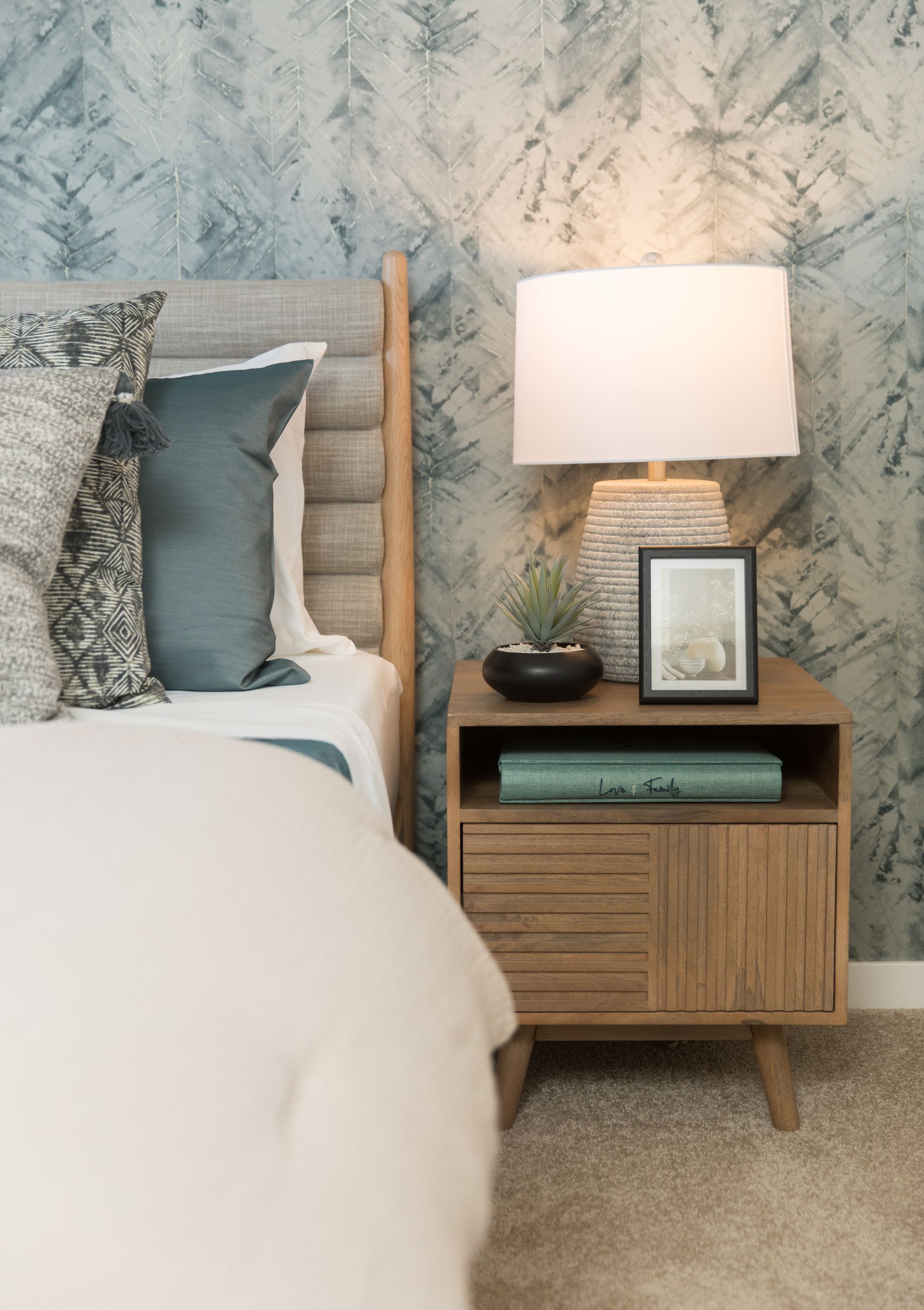 A bedroom with a bed , nightstand , lamp and picture frame.