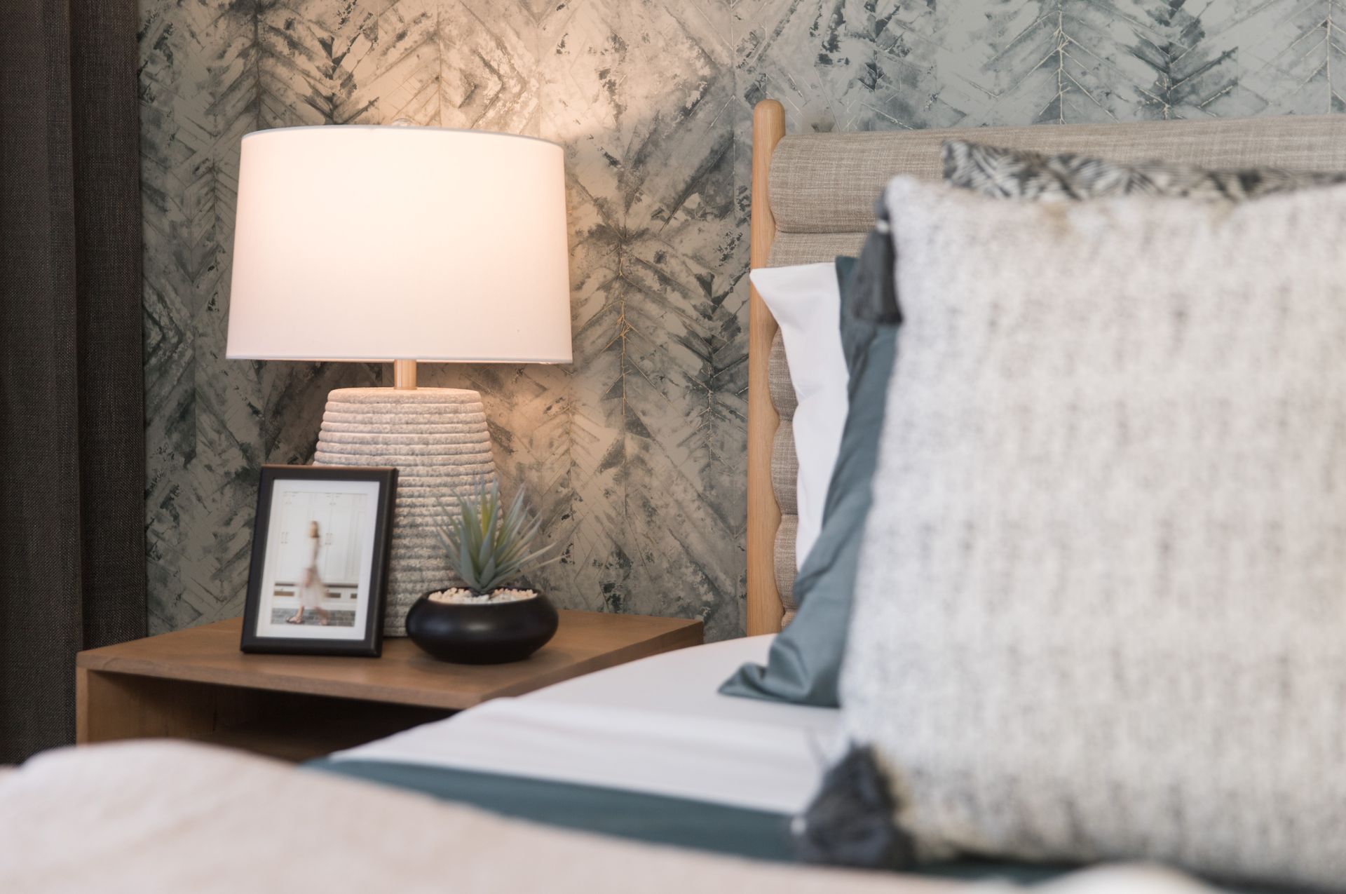 A bedroom with a bed , nightstand , lamp and picture frame.