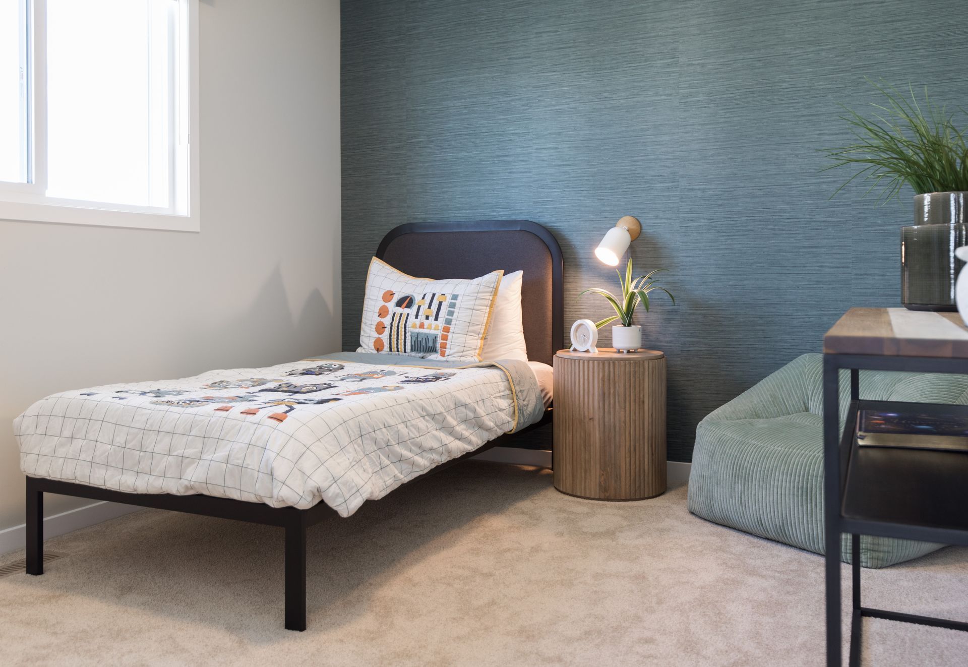 A bedroom with a single bed , nightstand , desk and window.