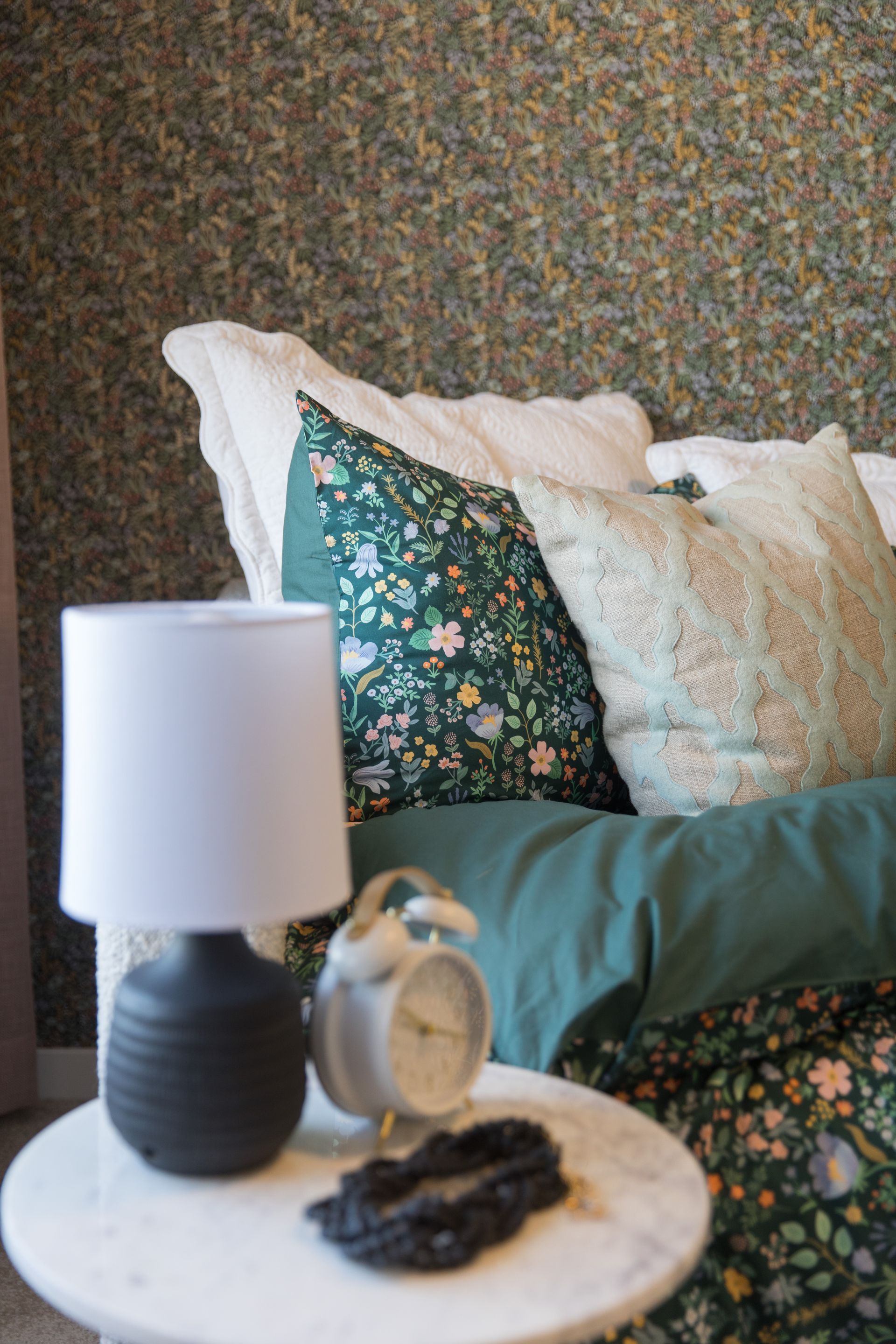A bedroom with a bed , nightstand , lamp and alarm clock.