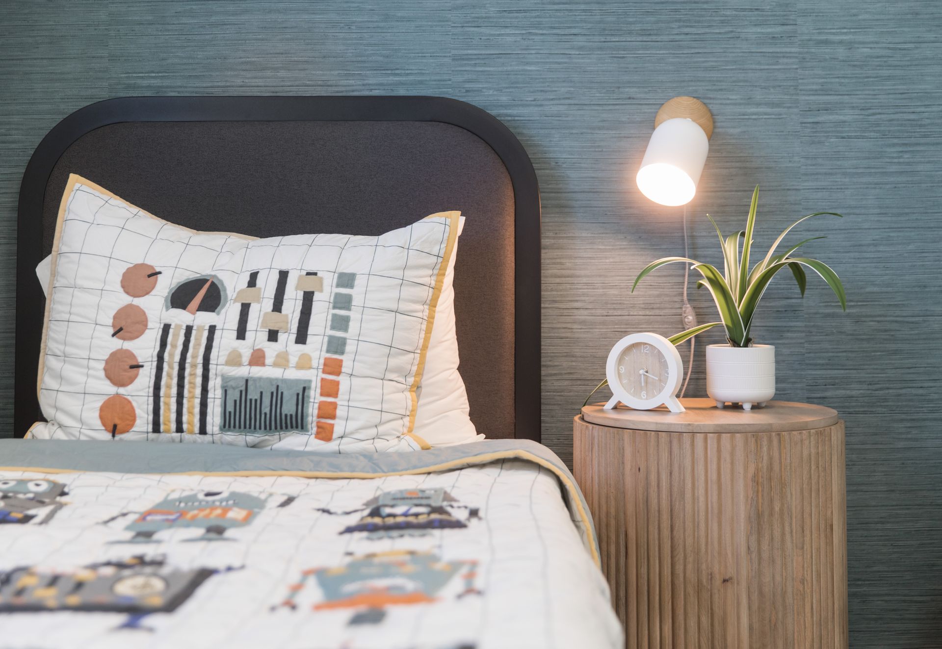 A bedroom with a bed , nightstand , lamp and plant.