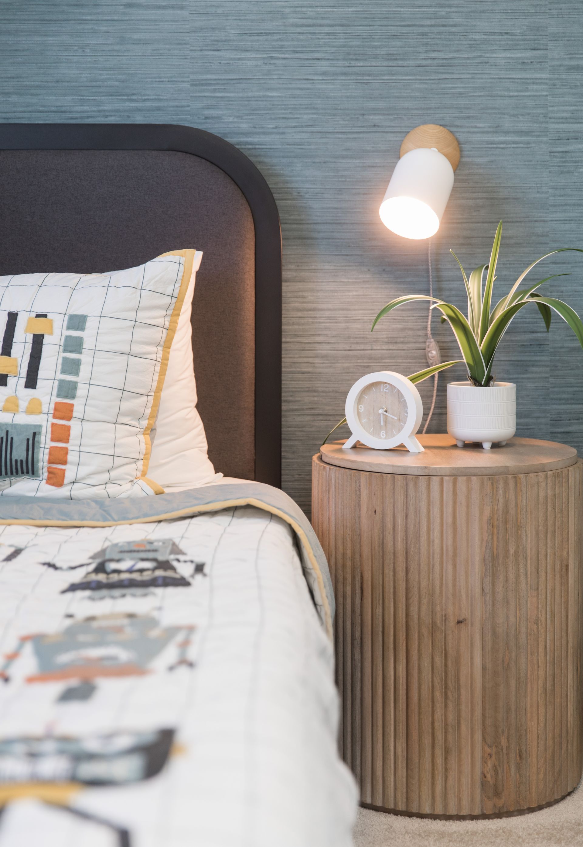A bedroom with a bed , nightstand , lamp and plant.