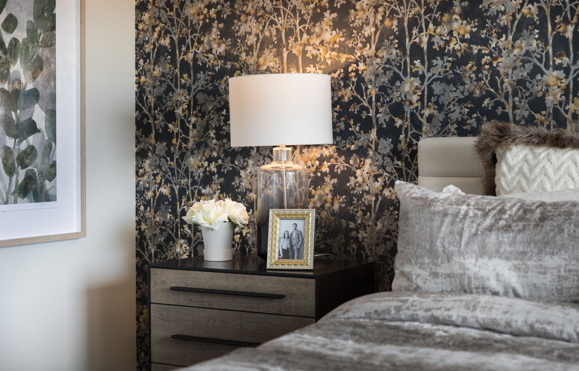 A bedroom with a bed , nightstand , lamp and picture on the nightstand.