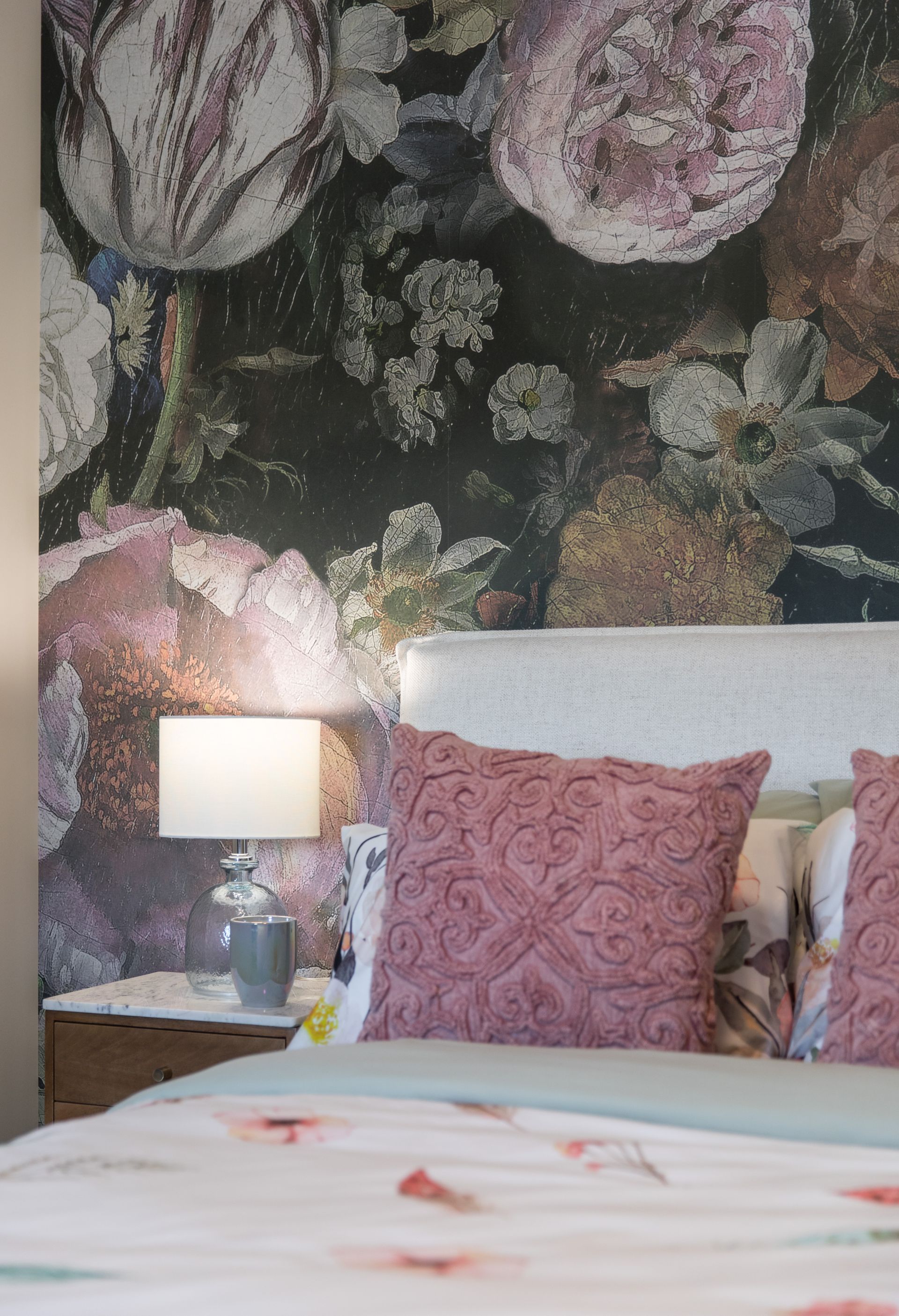 A bedroom with a bed , nightstand , lamp and floral wallpaper.
