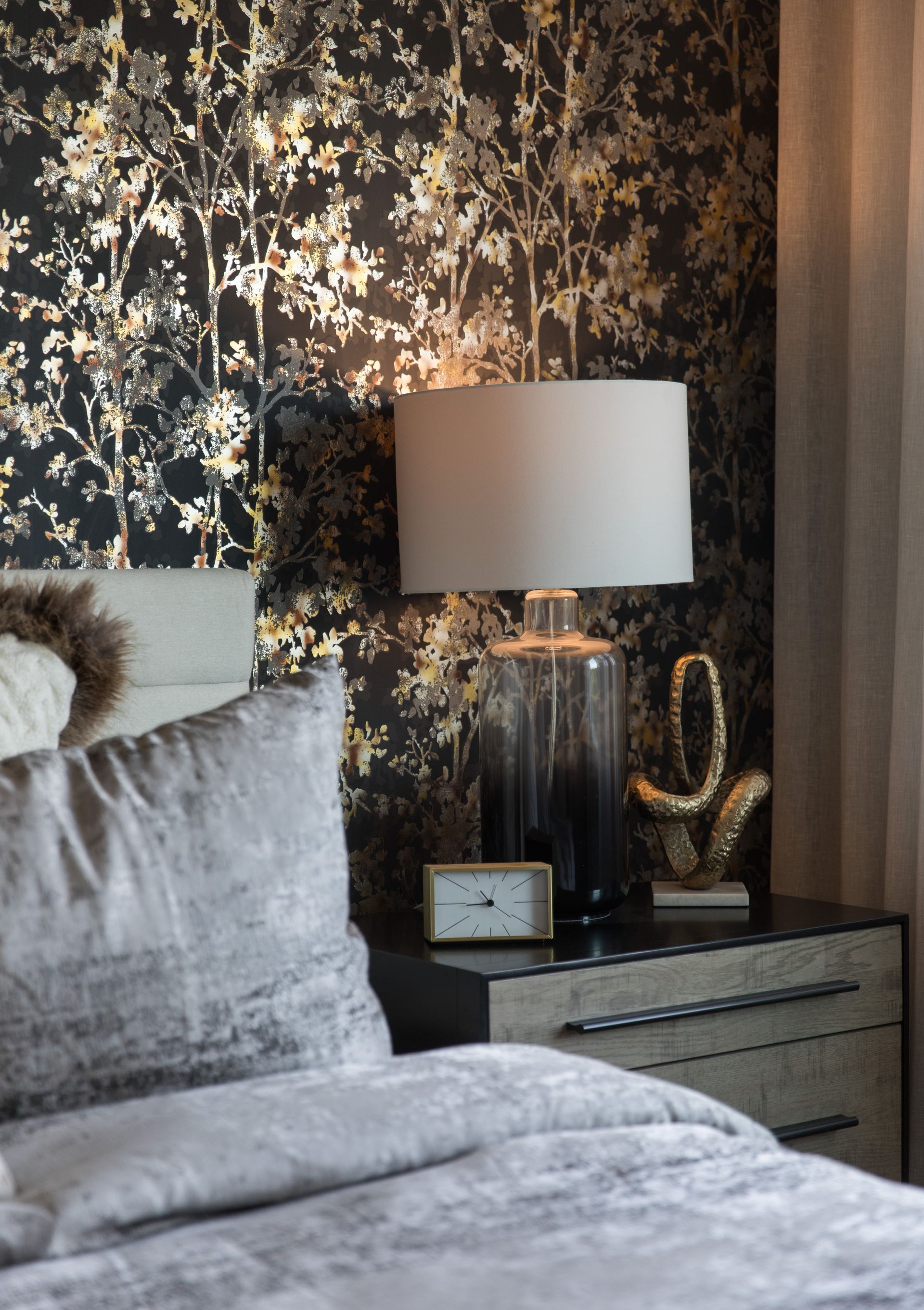 A bedroom with a bed , nightstand , lamp and clock.